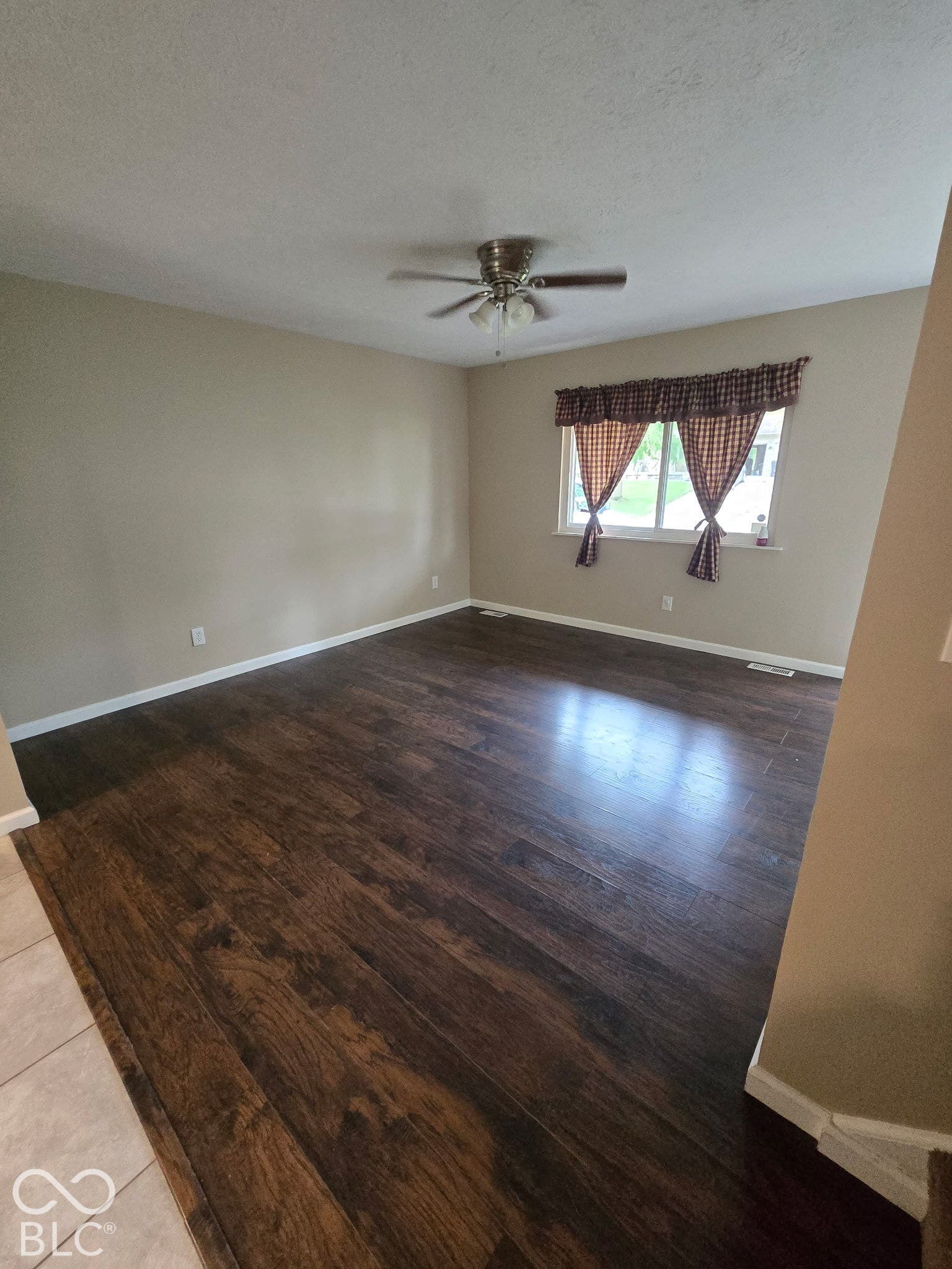 Dark wood-finish flooring, neutral wall paint, and a ceiling fan with integrated lighting