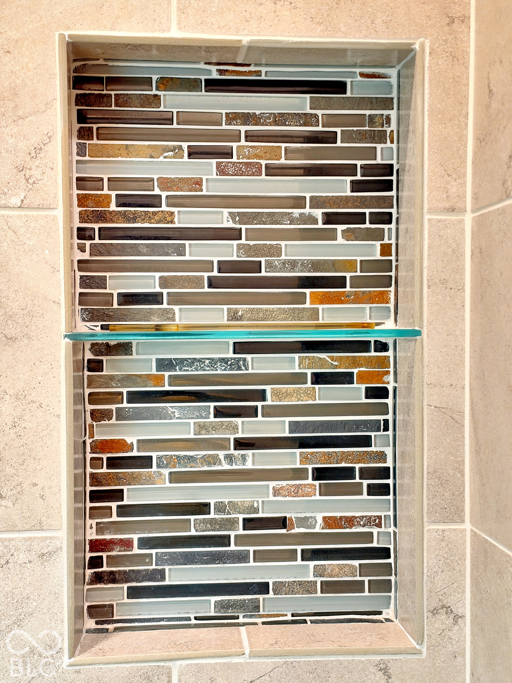 Recessed shower niche with glass and stone mosaic tile, featuring a clear glass shelf and neutral-toned perimeter tile surround