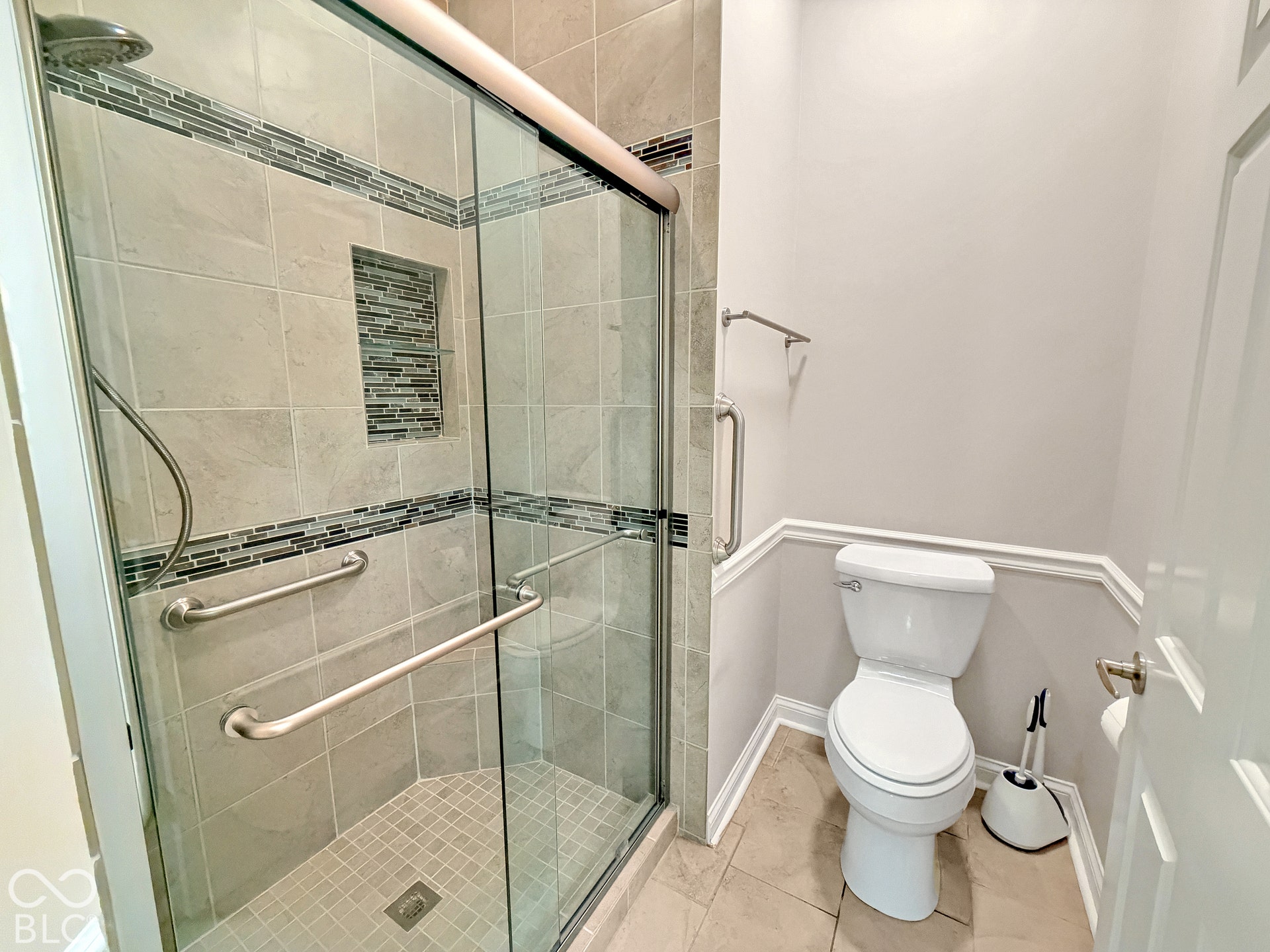 Tiled shower with glass enclosure, recessed shelf, and grab bars
