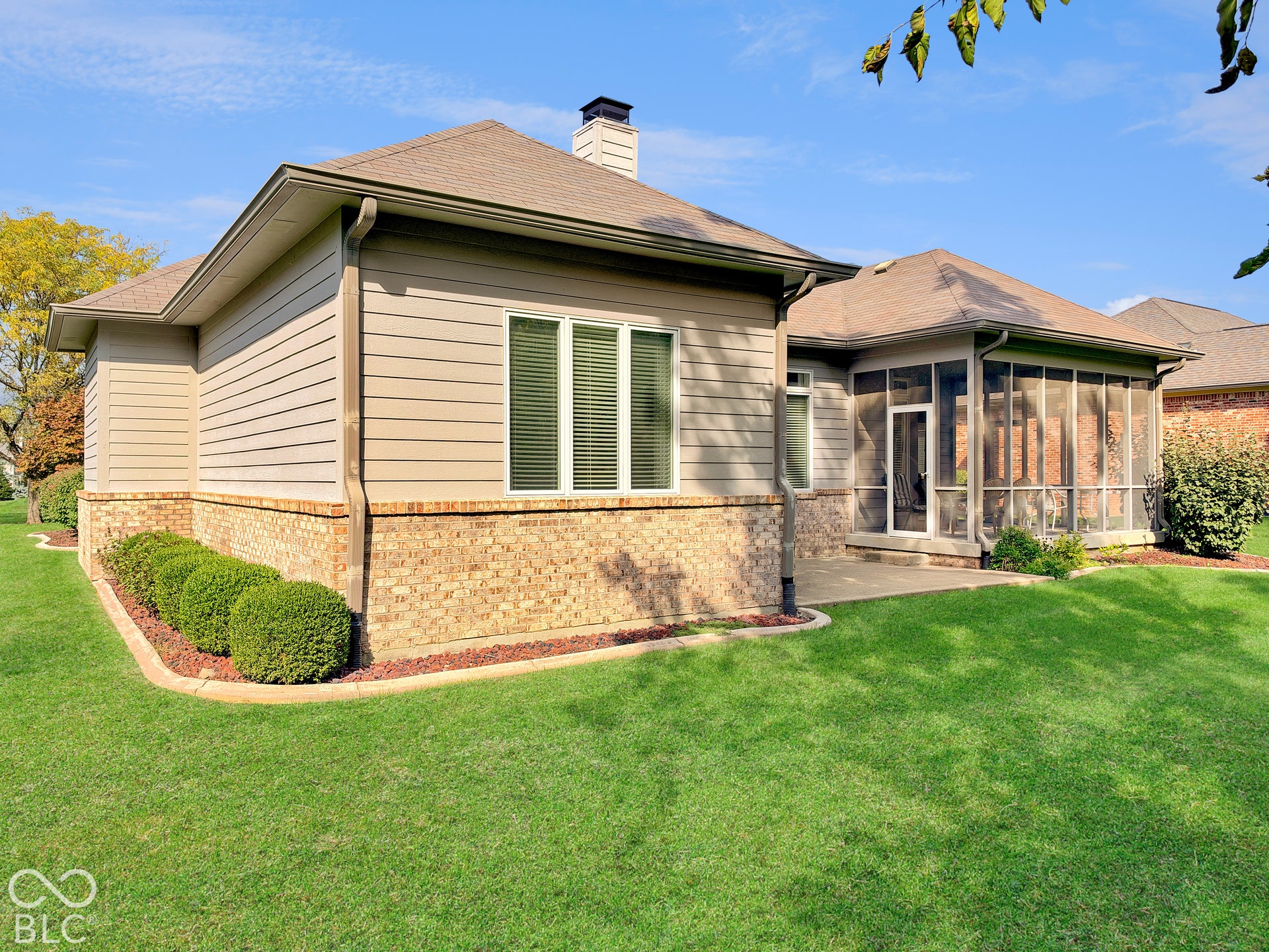 Back of home with screened-in porch with a concrete patio, brick and siding exterior, and landscaped perimeter plantings.