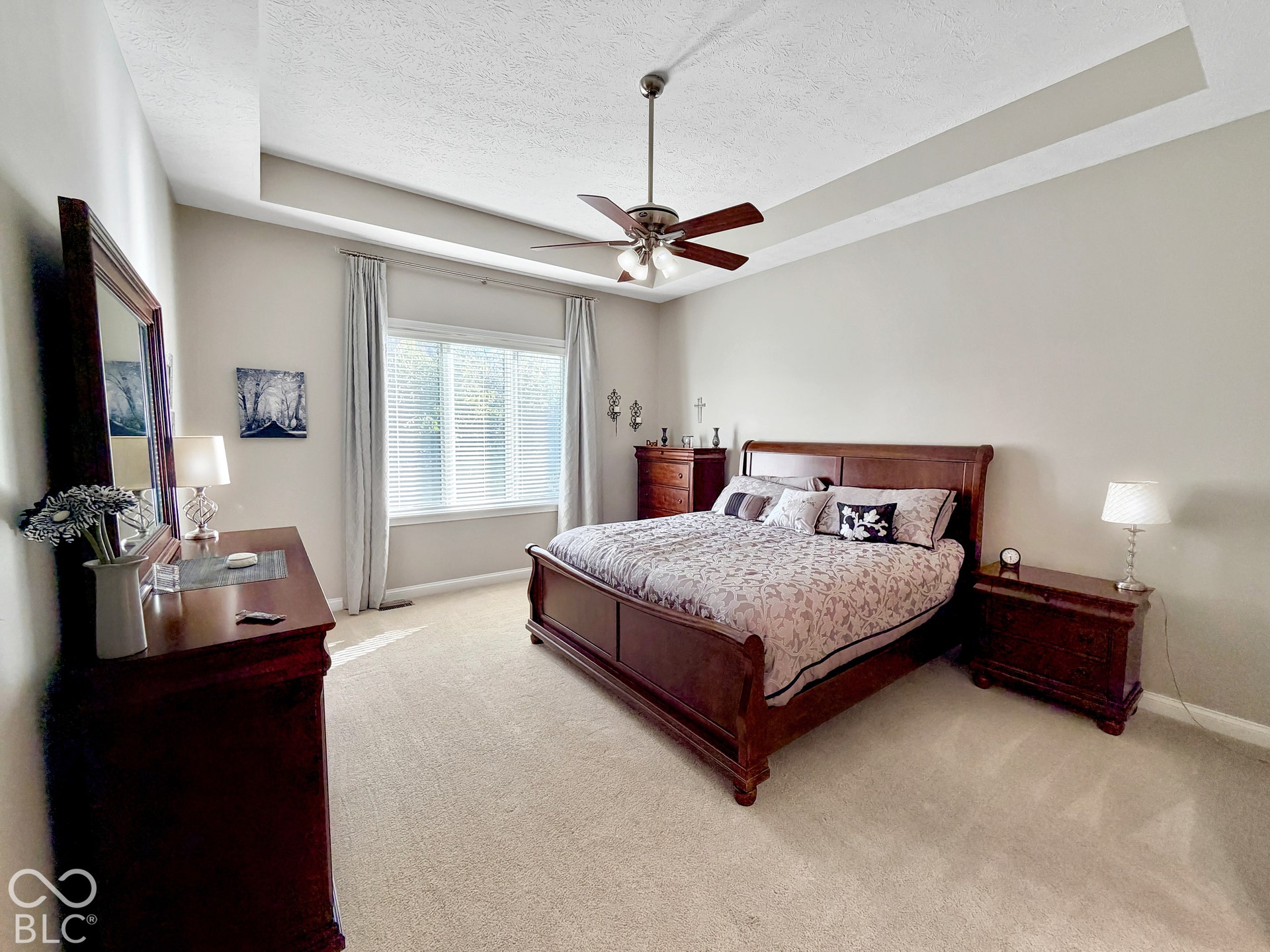 Tray ceiling with crown molding, ceiling fan, large window with blinds, light-toned carpeting, and neutral wall paint