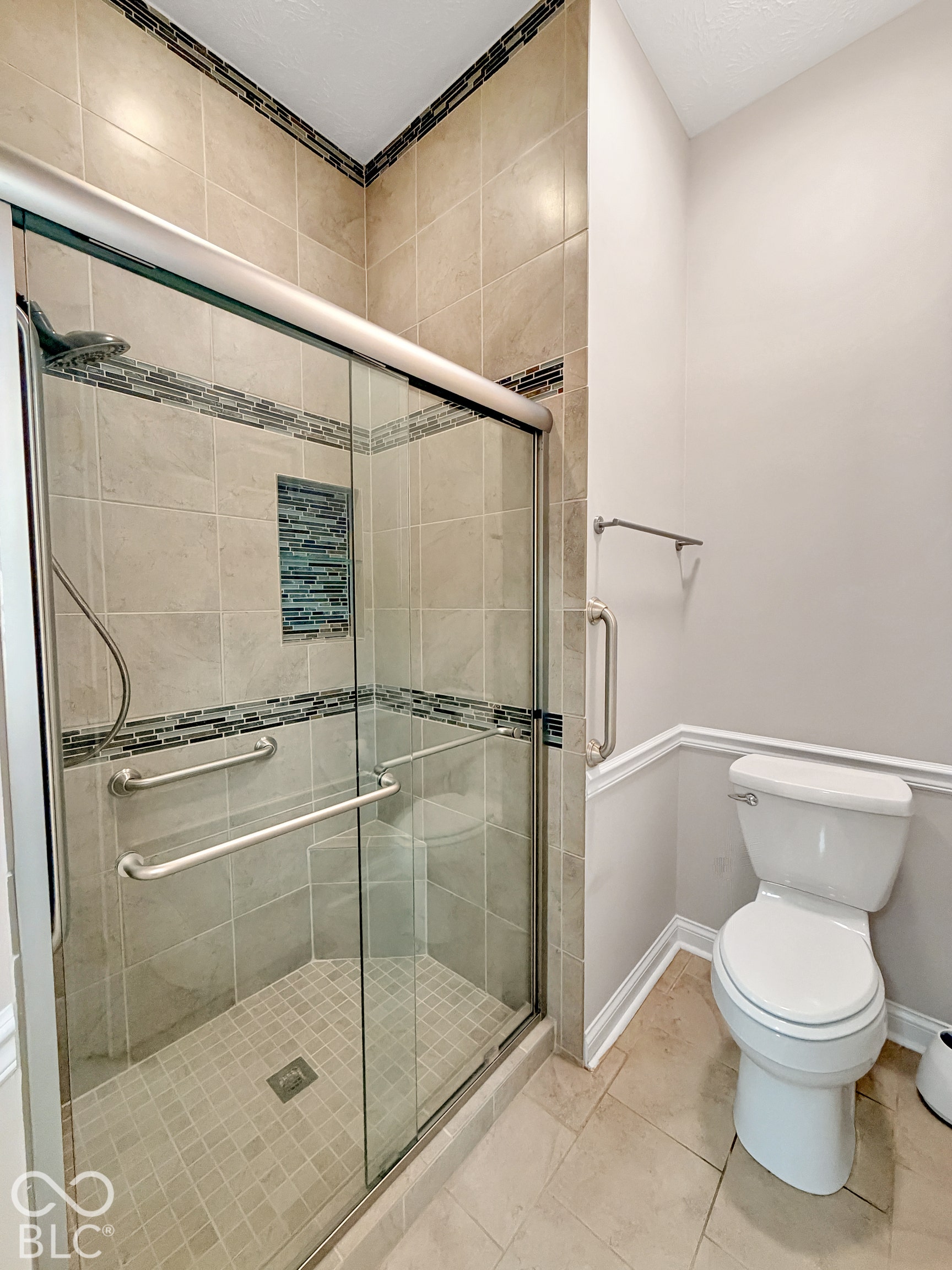 Tiled shower with glass enclosure, mosaic accent tile, and stainless steel grab bars