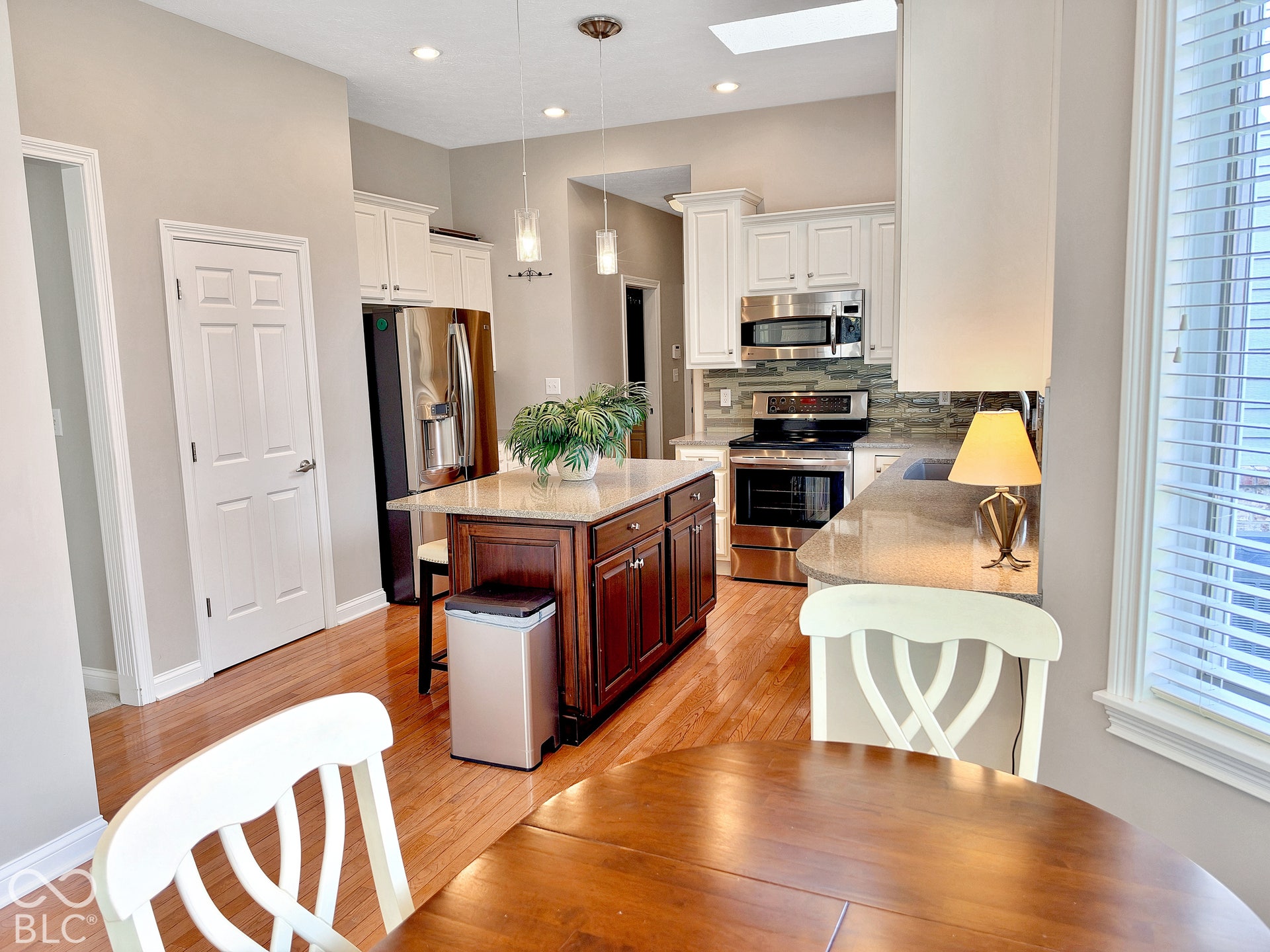 Kitchen featuring wood-finish flooring, white cabinetry, a central island with a contrasting wood finish, stainless steel appliances, and a tile backsplash