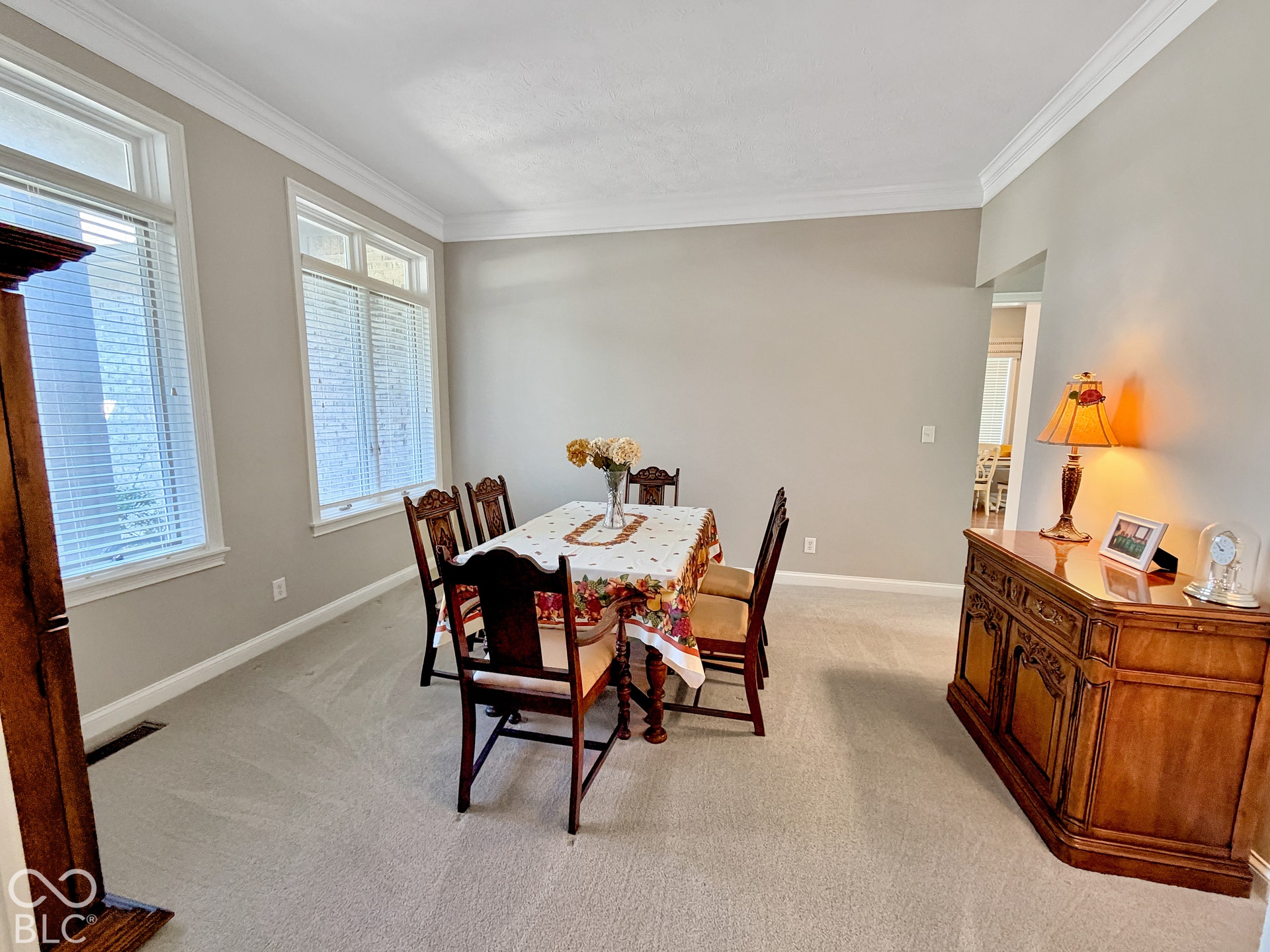 Dining room with neutral wall paint with crown molding and white trim, light-toned carpeting, and lots of natural light.