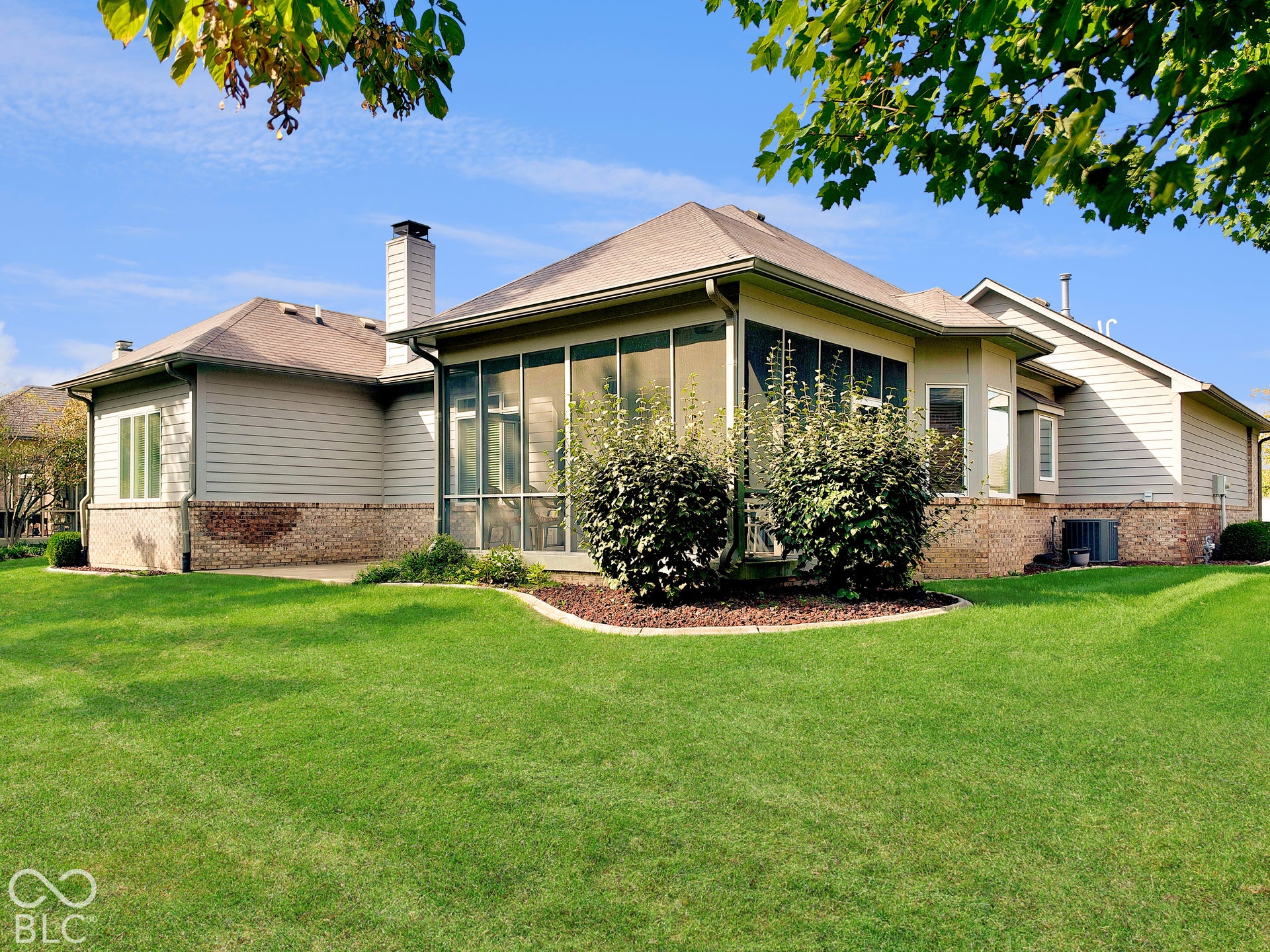 Rear exterior of home with lawn and mature landscaping, screened enclosure, and brick-accented siding.