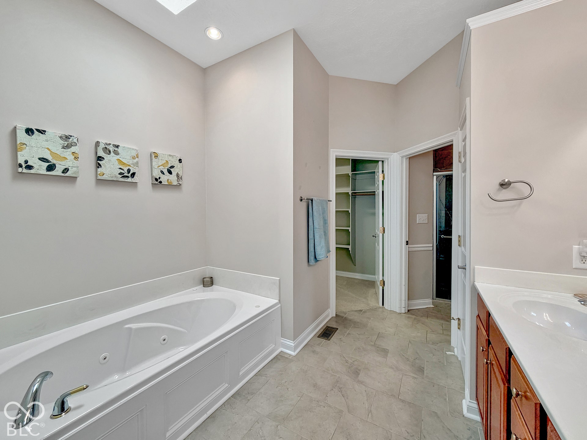 Recessed soaking tub with integrated jets, skylight, tile flooring, and double vanity with wood-finish cabinetry