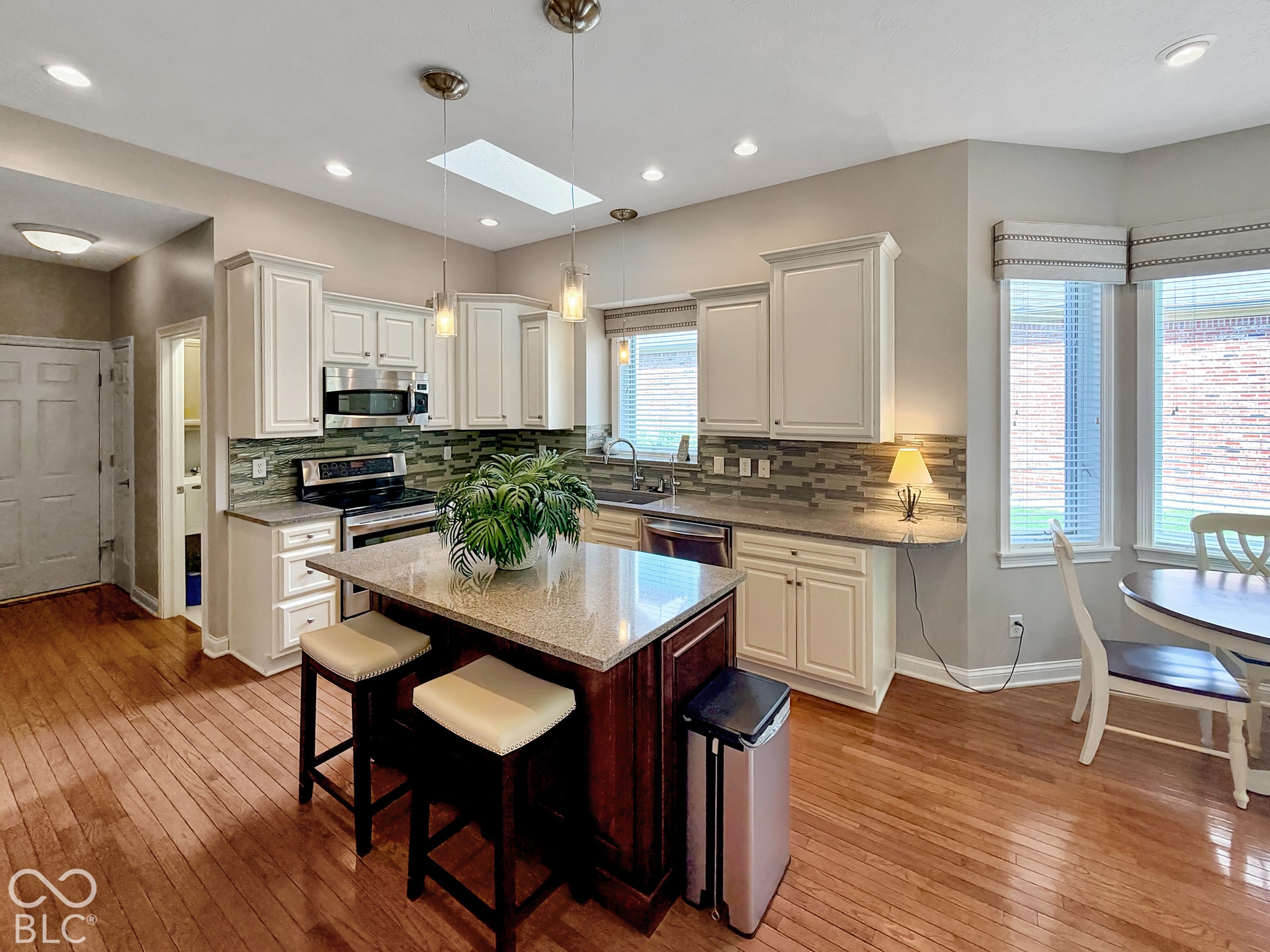 Kitchen featuring wood-finish flooring, white cabinetry, a central island with countertop seating, stainless steel appliances, and a skylight