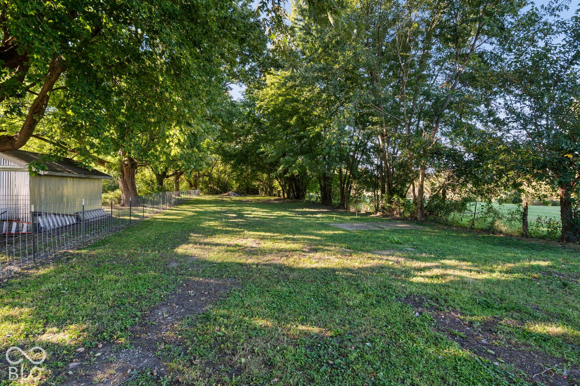 Expansive grassy area with mature trees and a utility structure