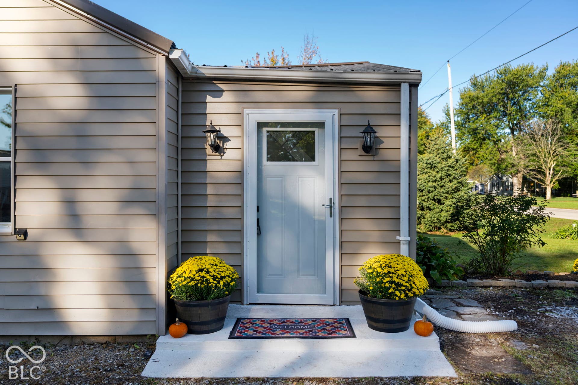 Entryway featuring a white door with upper window, two outdoor wall lanterns, horizontal siding, and a concrete stoop