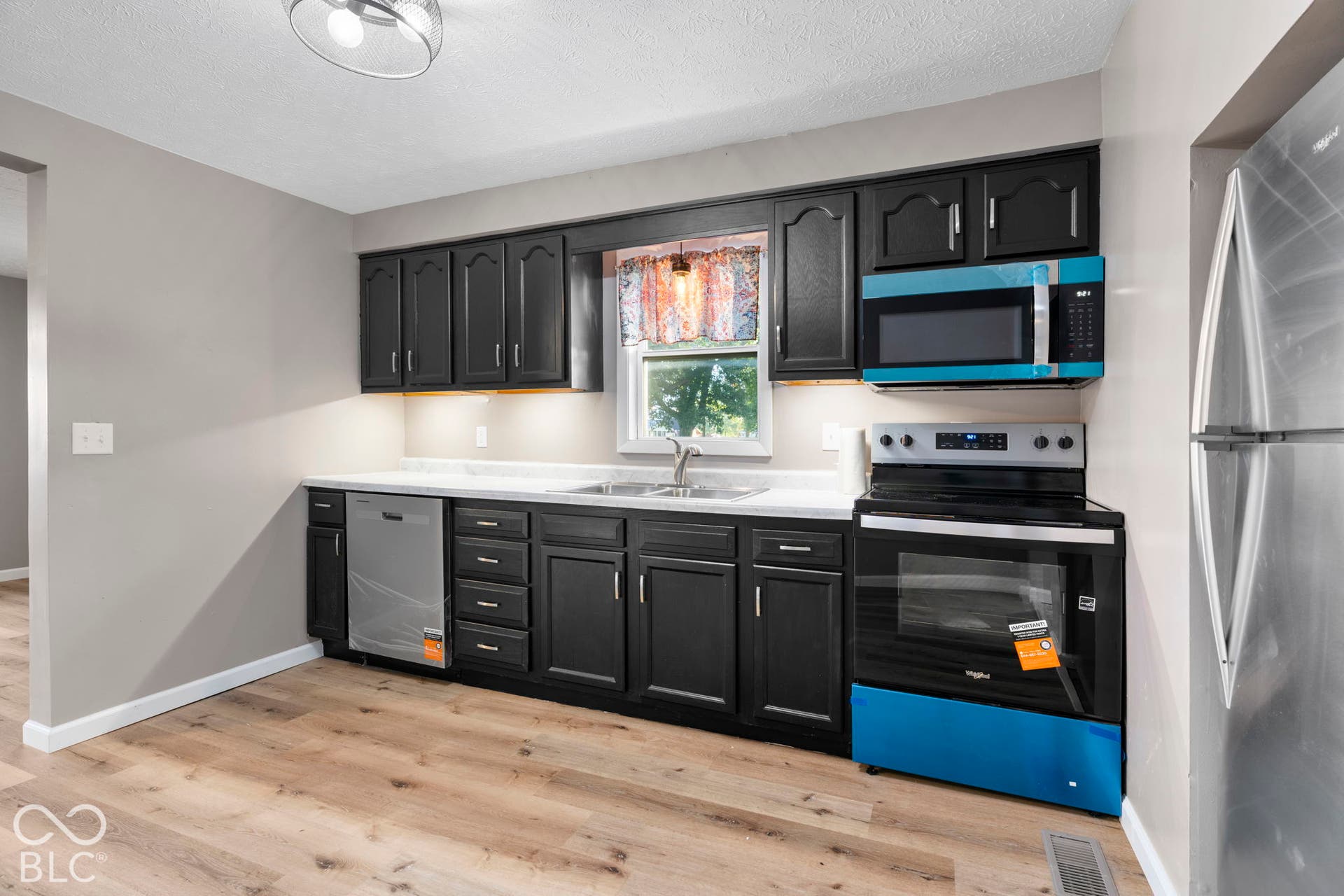Kitchen featuring black cabinetry, light-toned countertops, a stainless steel dishwasher, and a built-in microwave