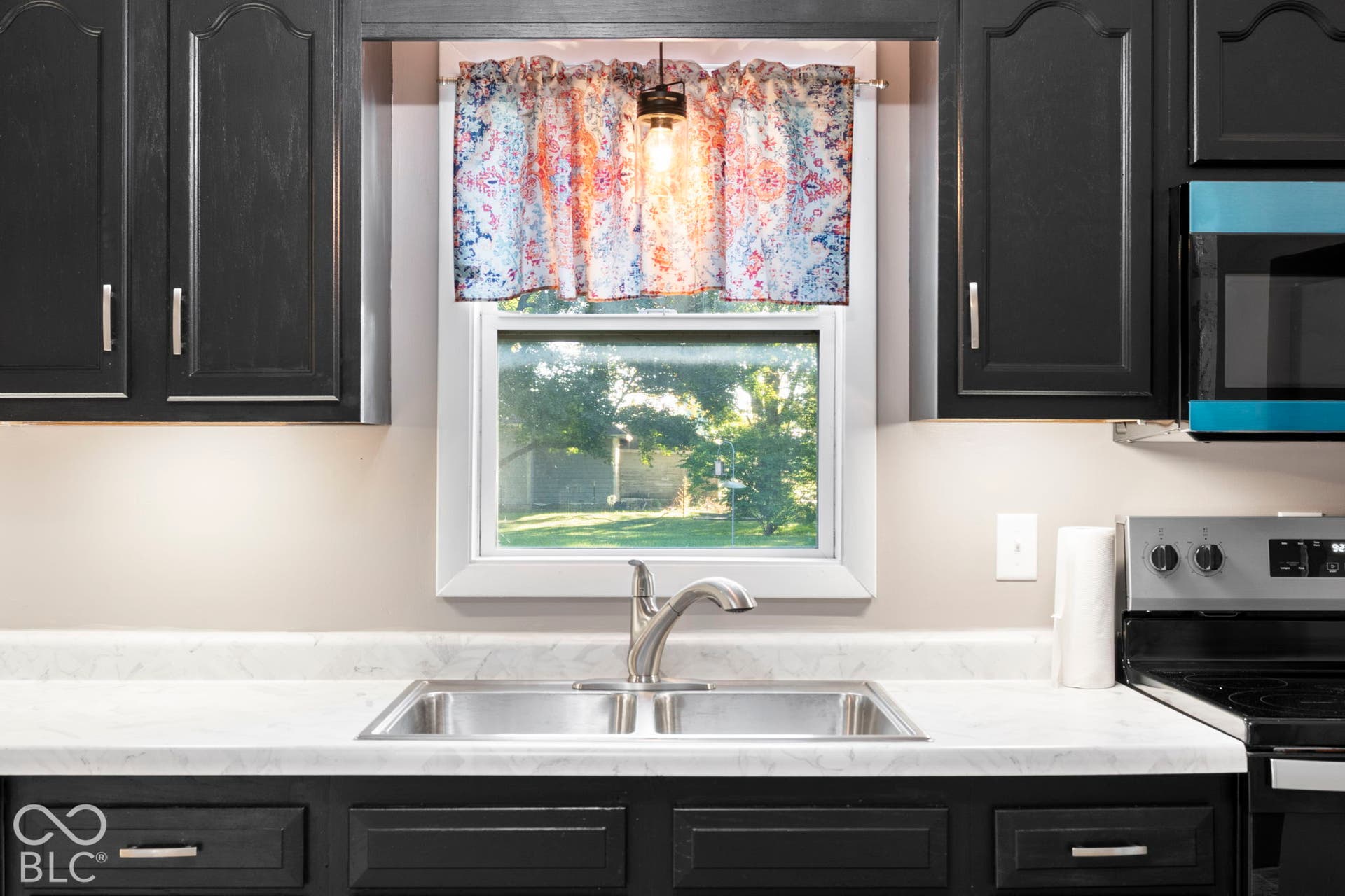 Stainless steel double basin sink with a chrome faucet, white countertop, dark cabinetry with bar pull hardware, and built-in microwave
