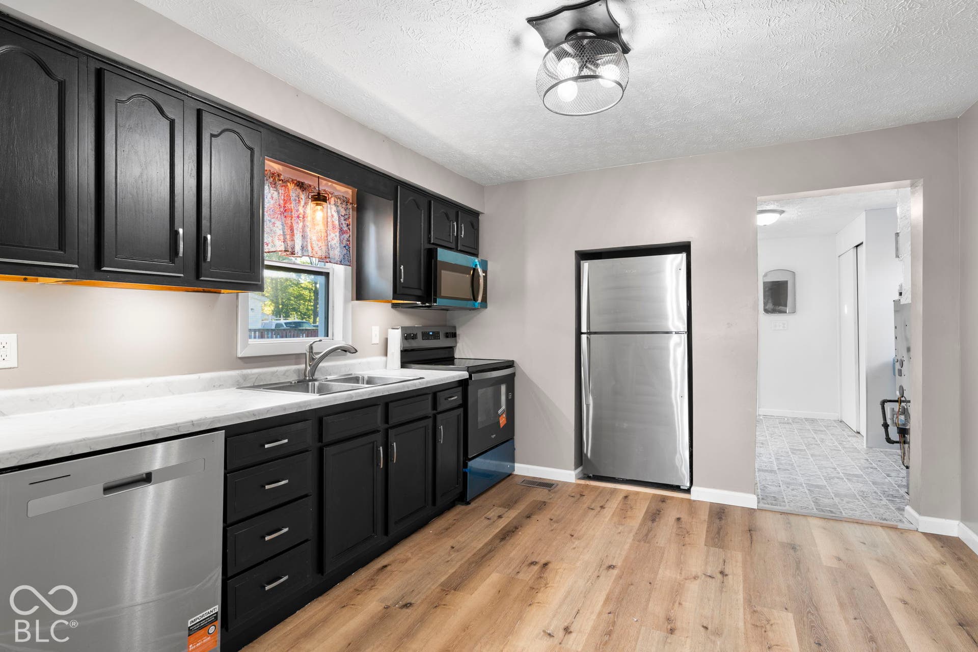 Kitchen featuring dark cabinetry, stainless steel appliances, light-toned countertops, wood-finish flooring, and a contemporary ceiling fixture