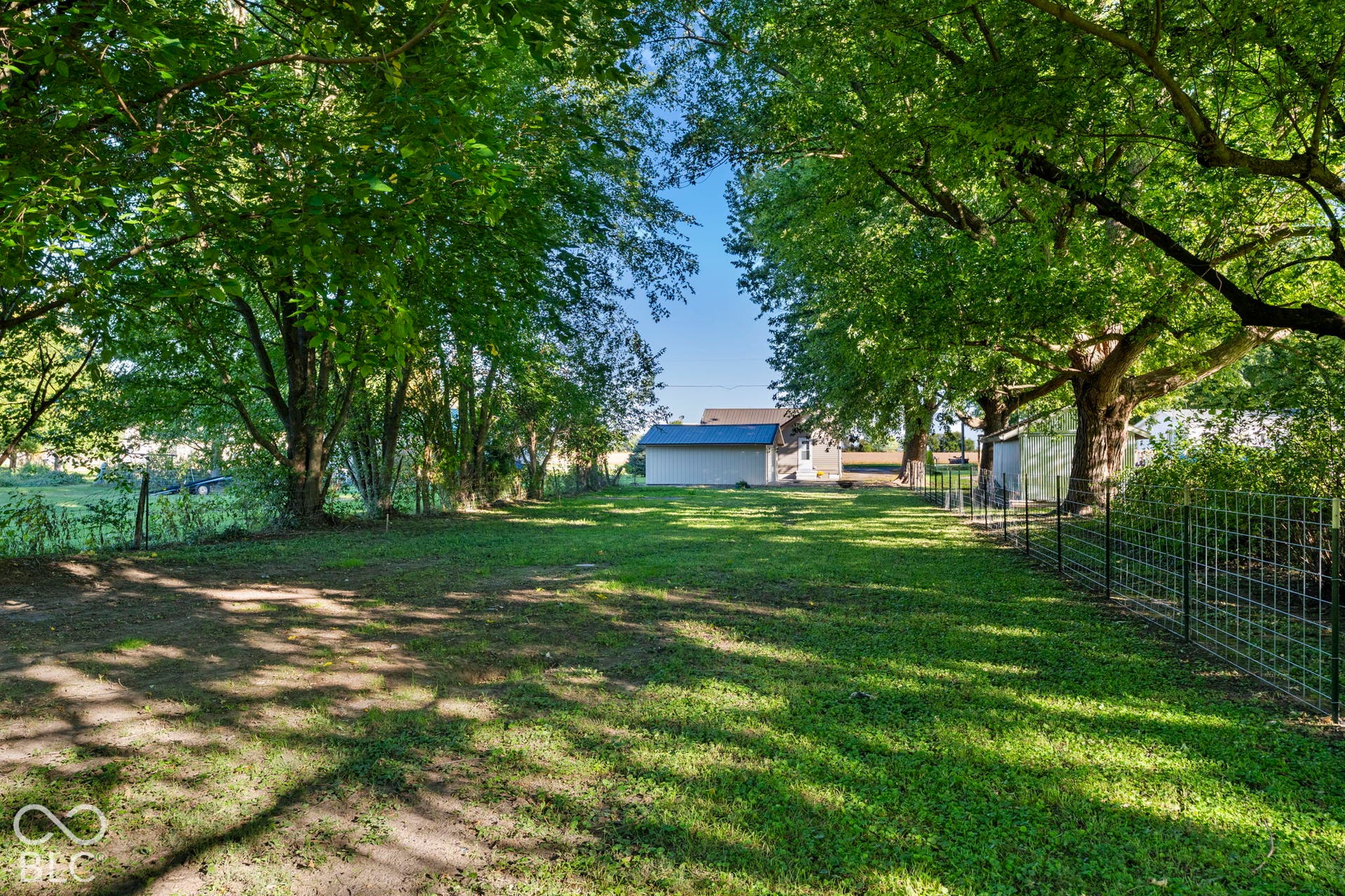 Expansive grassed area featuring mature trees and a wire fence
