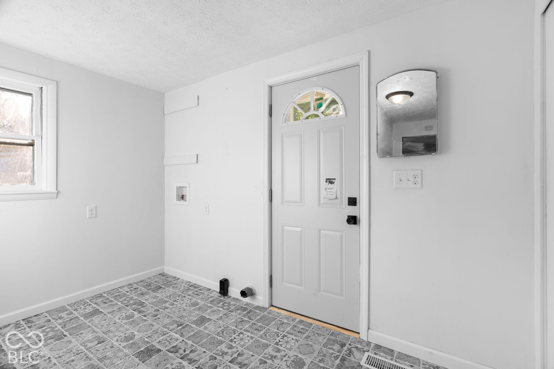 White paneled door with an arched glass insert, window with white trim, and patterned tile flooring