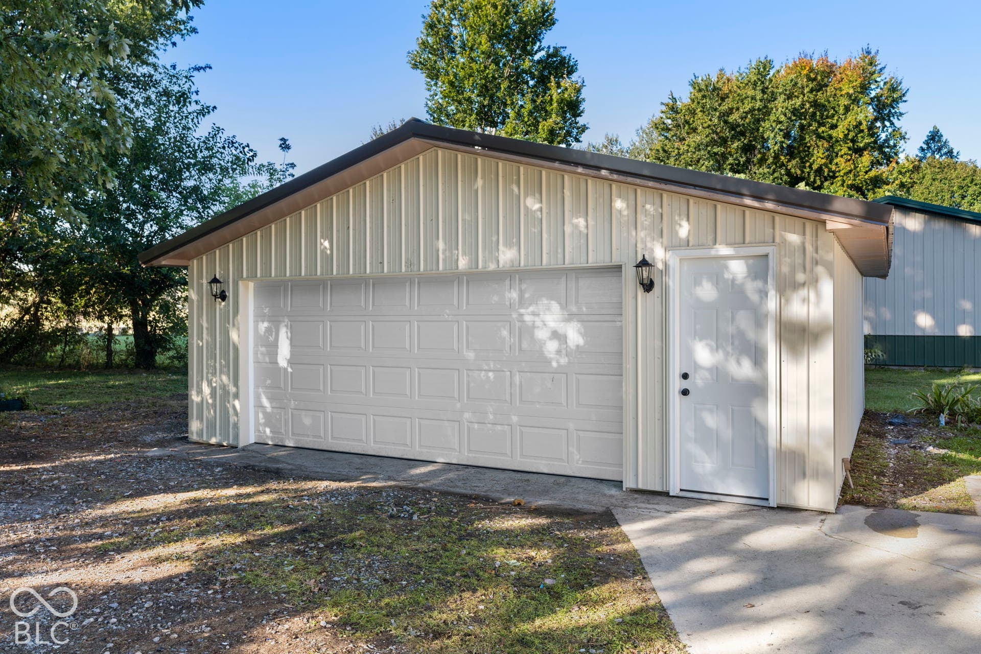 Detached garage structure with a panel-style overhead door, a pedestrian entry door, and exterior sconce lighting