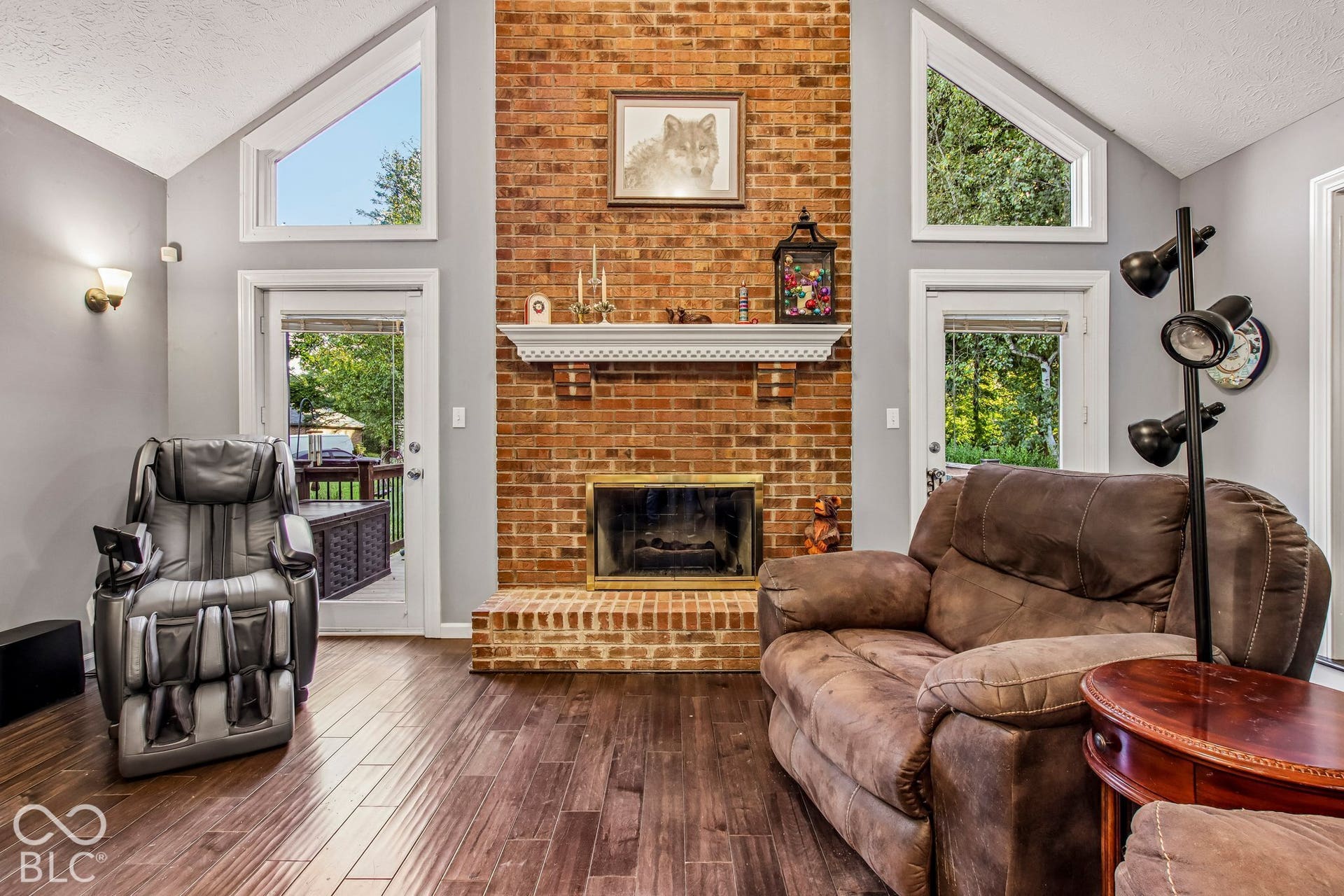 View of living room with 16' ceiling, updated laminate hardwood flooring, floor to ceiling brick fireplace and 2 separate doors leading to deck and back yard
