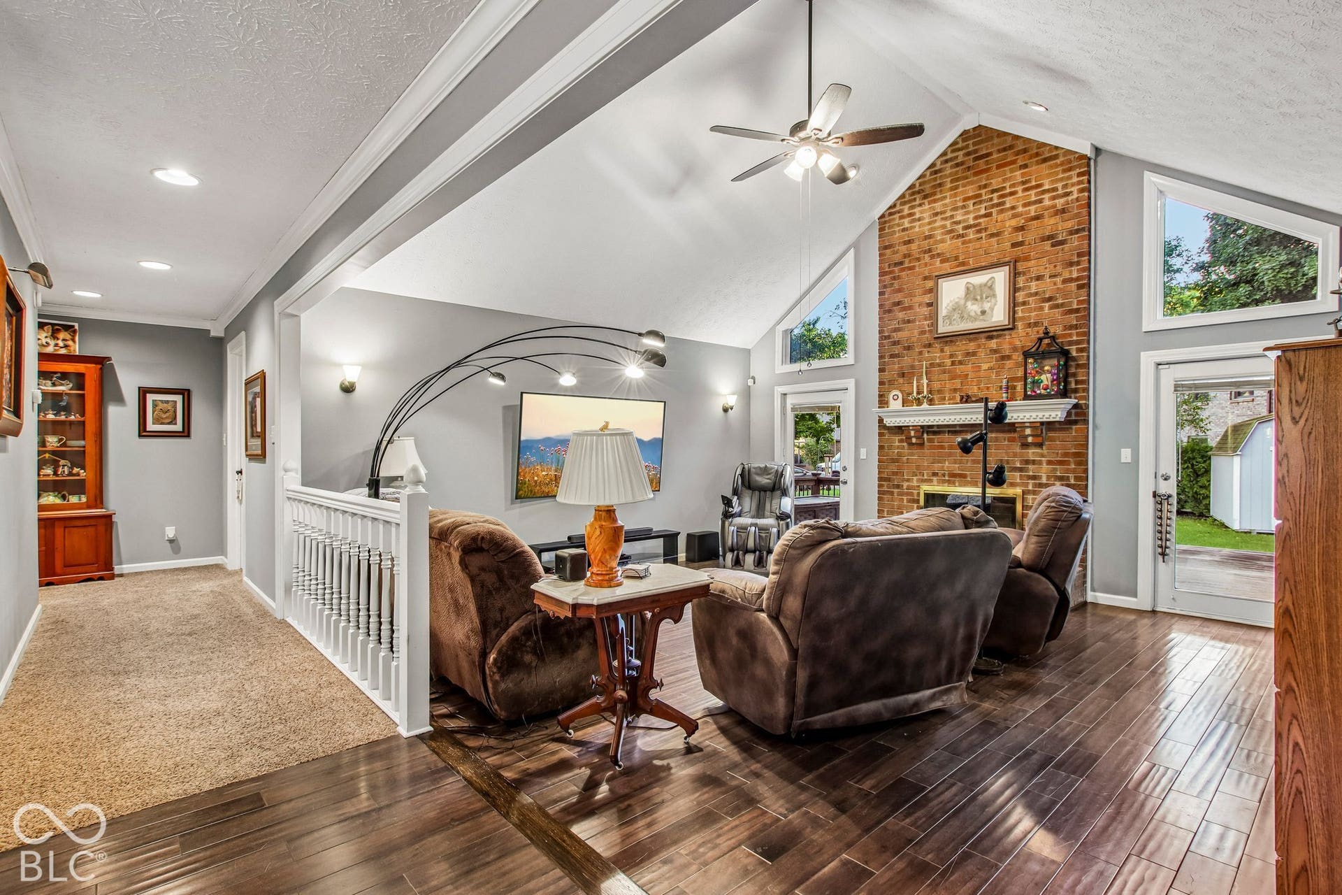 View of living room with 16' ceiling, updated laminate hardwood flooring, floor to ceiling brick fireplace and 2 separate doors leading to deck and back yard
