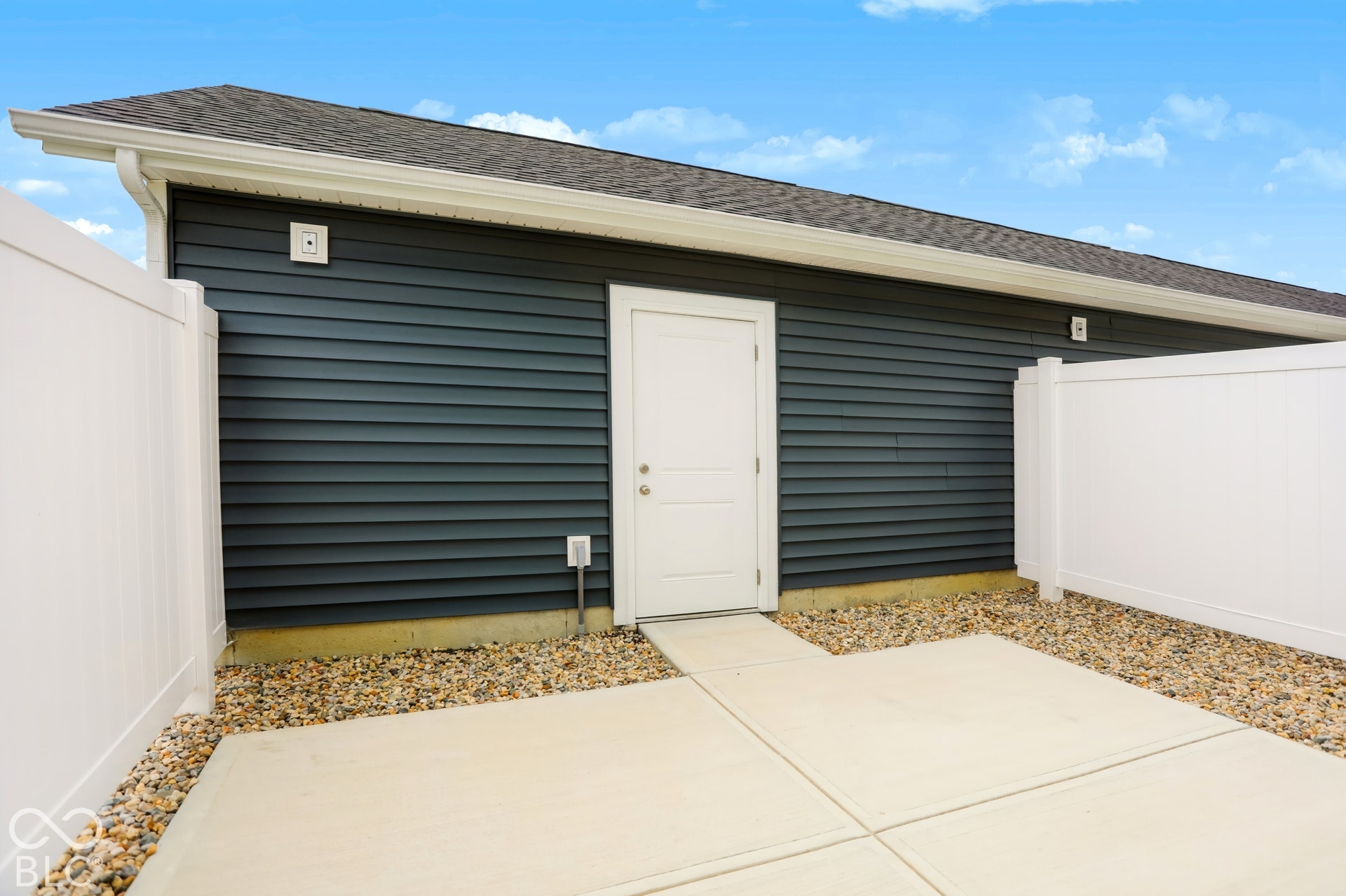 Private patio area featuring concrete paving, gravel landscaping, and white vinyl fencing