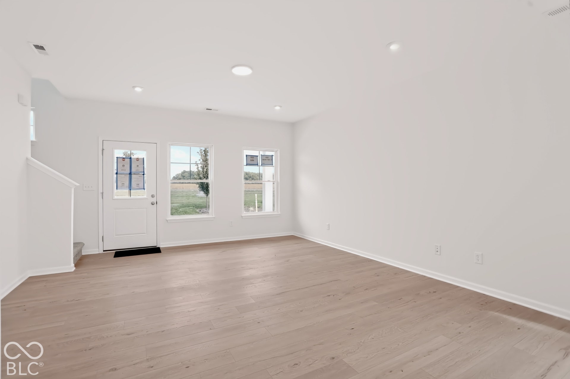 Wood-finish flooring, white walls, recessed ceiling lighting, rear entry door, and two windows