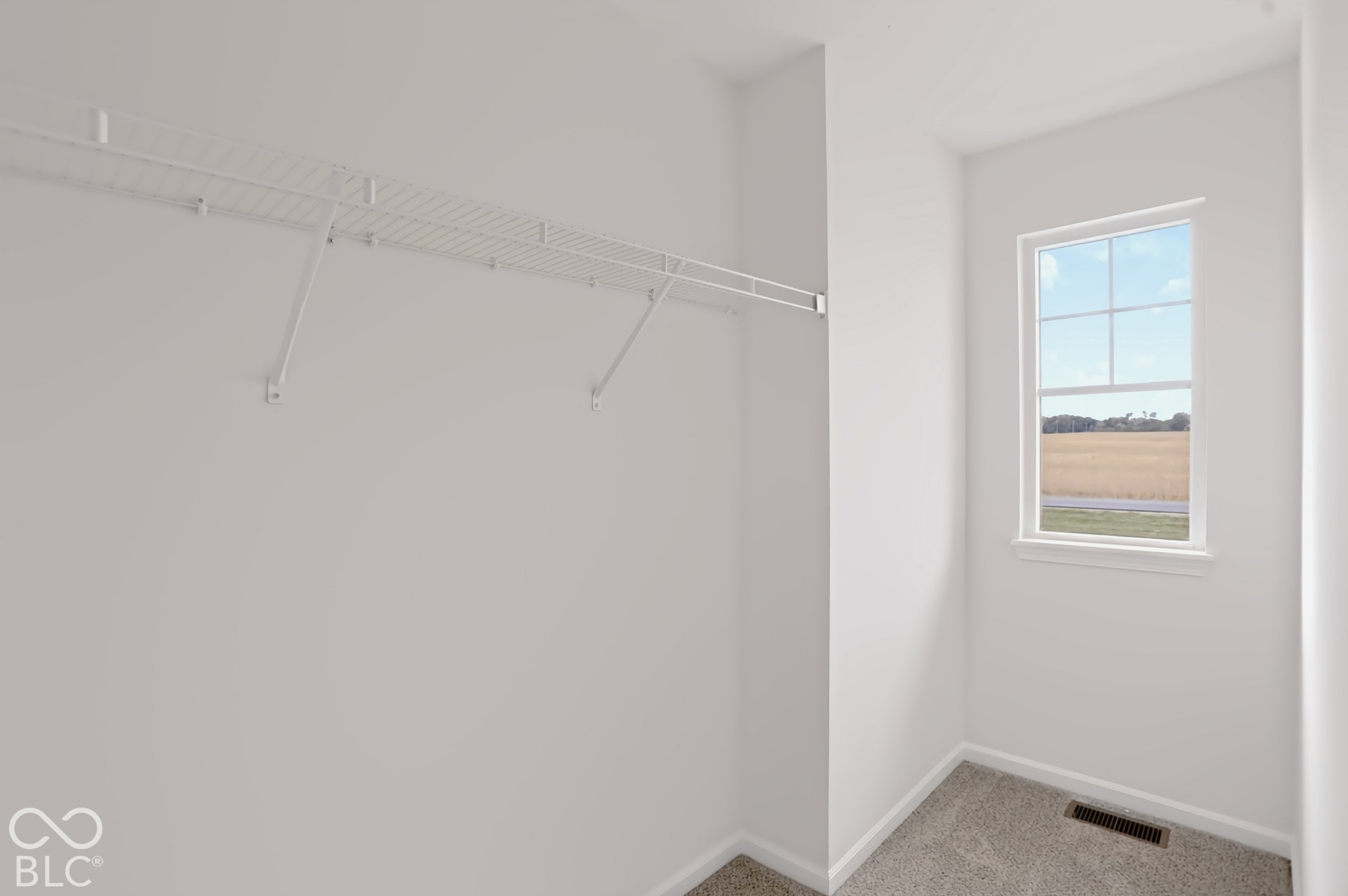 Windowed interior space with light gray wall-to-wall carpeting and a white wire shelving system