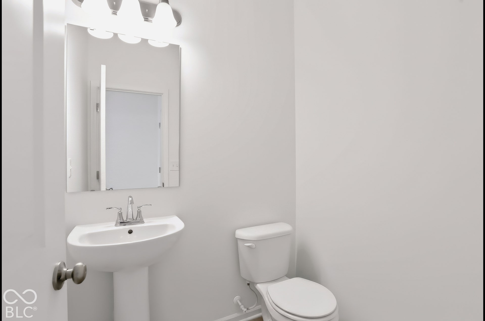 Pedestal sink with chrome faucet, wall-mounted mirror, and overhead vanity lighting