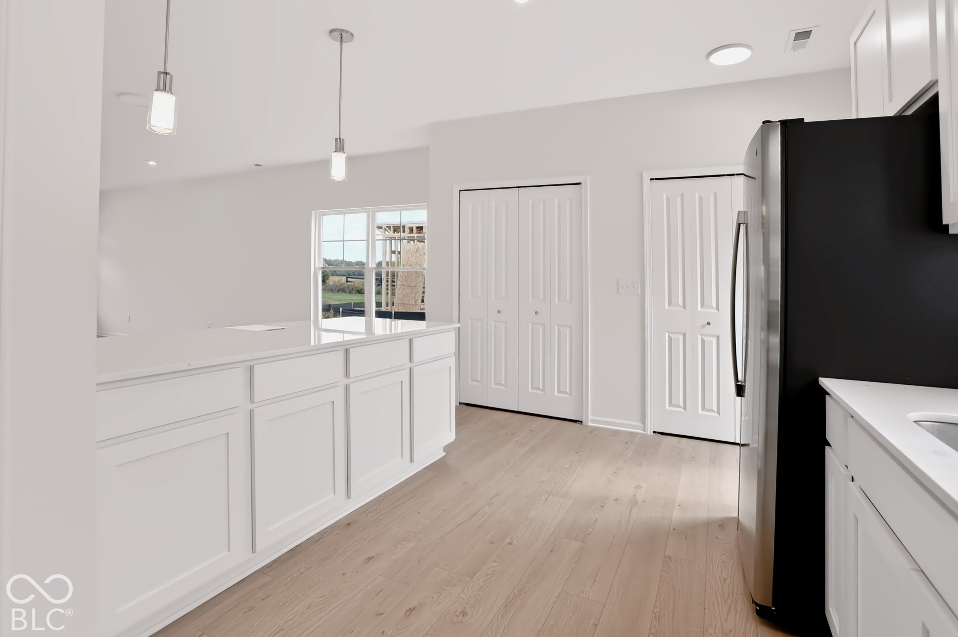 Kitchen featuring wood-finish flooring, white cabinetry, a kitchen island with pendant lighting, a stainless steel refrigerator, and a sliding glass door