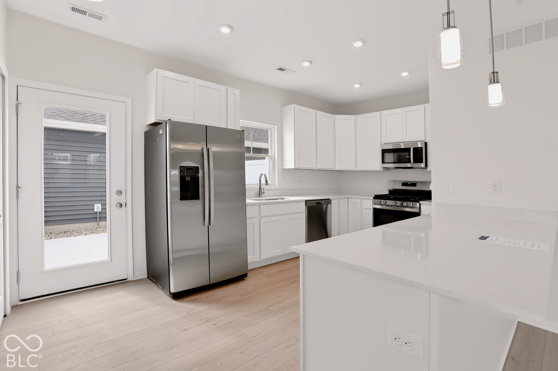 Kitchen featuring stainless steel appliances, white cabinetry, a large kitchen island with counter seating, light wood-finish flooring, and recessed lighting