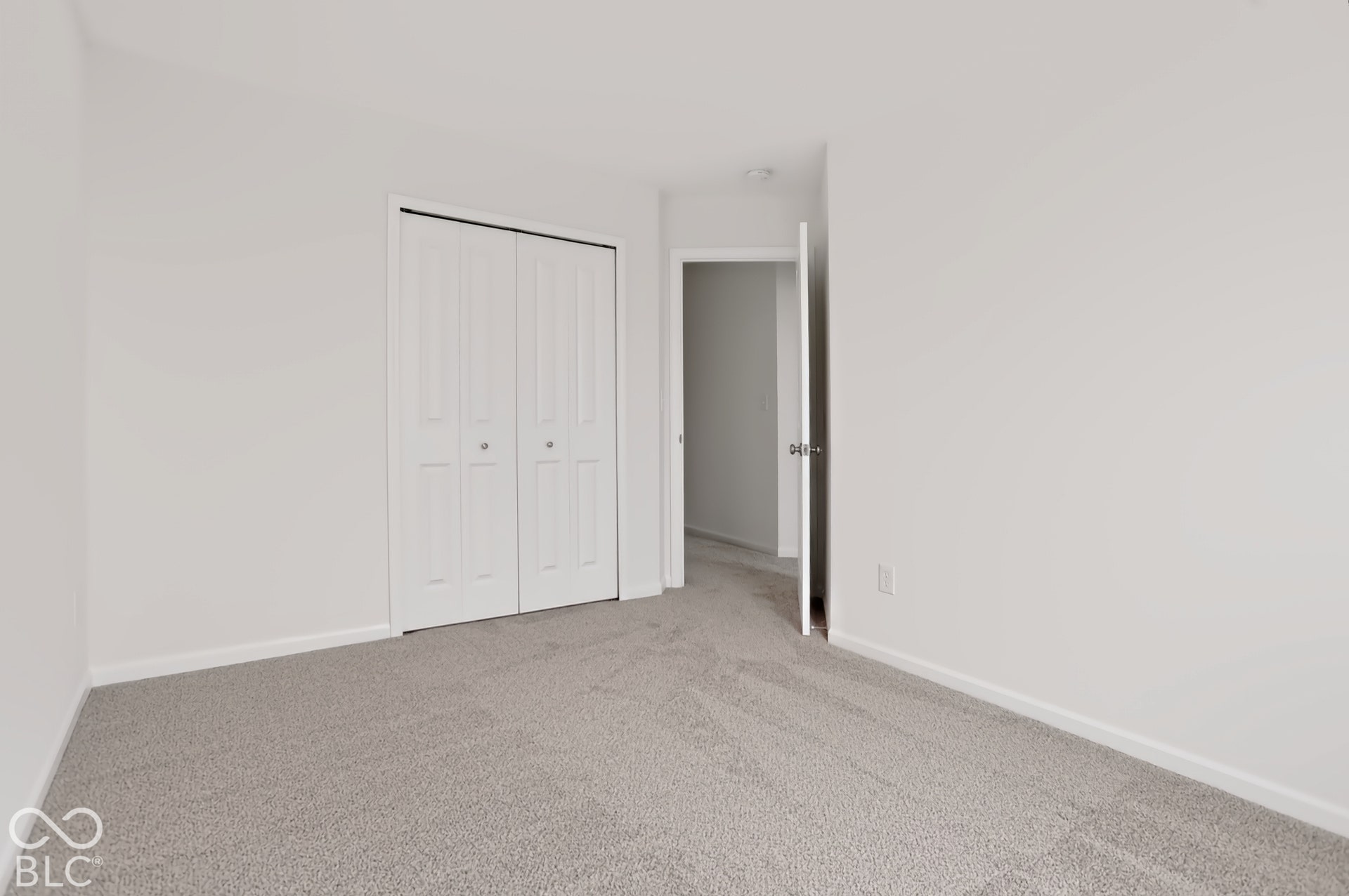 Neutral-toned carpeting complemented by white walls and trim, featuring a white bi-fold closet door and an open doorway