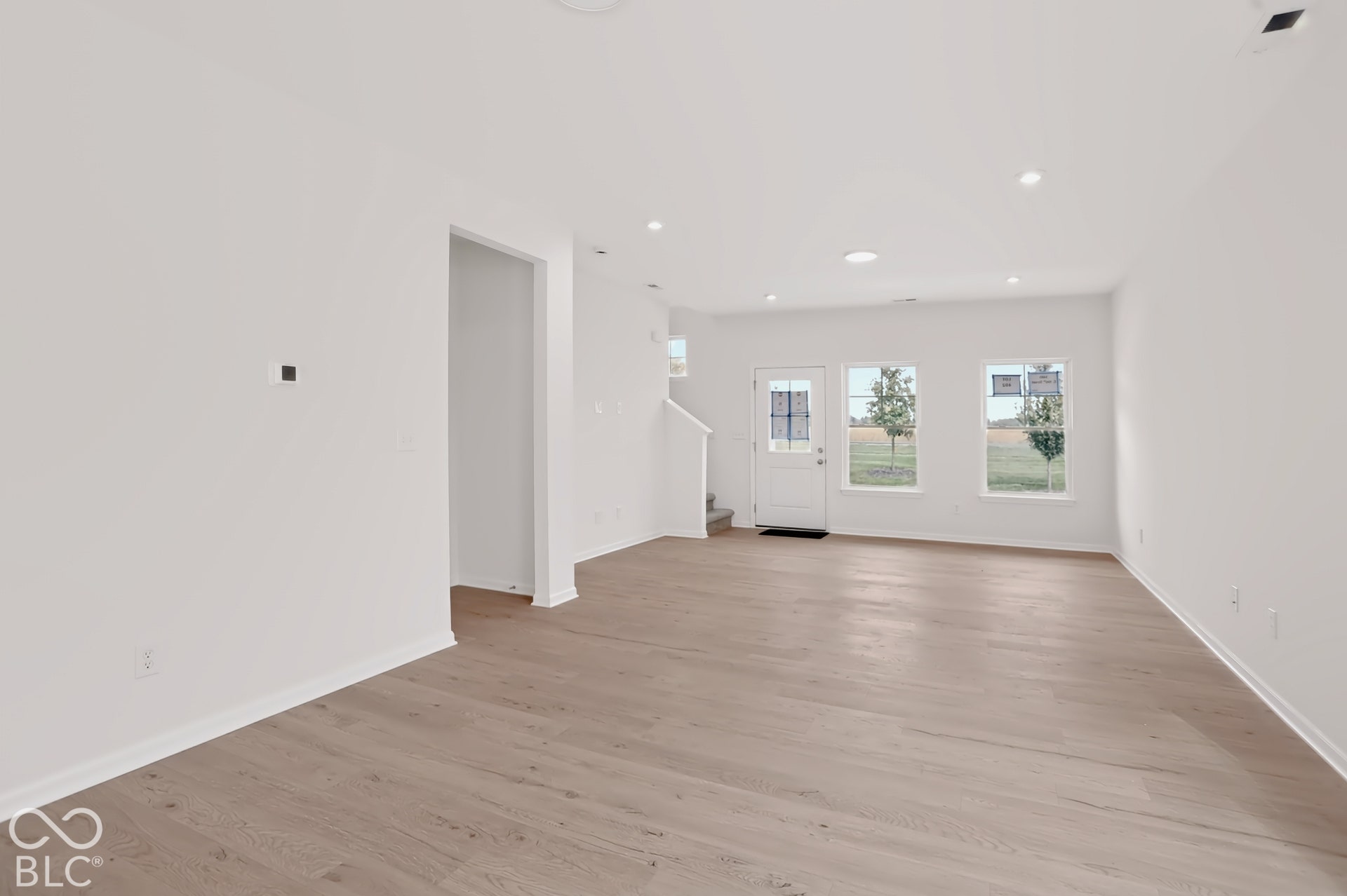 Light wood-finish flooring throughout, white walls, recessed ceiling lighting, and a white door with multiple window panes