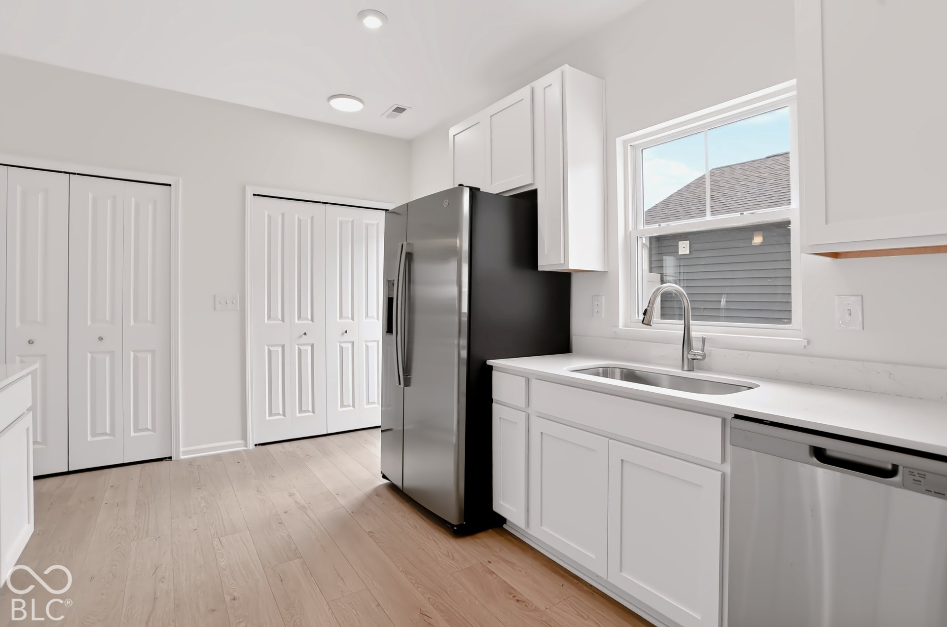 White shaker cabinetry, light-tone wood-finish flooring, stainless steel appliances, white countertops, and a stainless steel sink with a gooseneck faucet