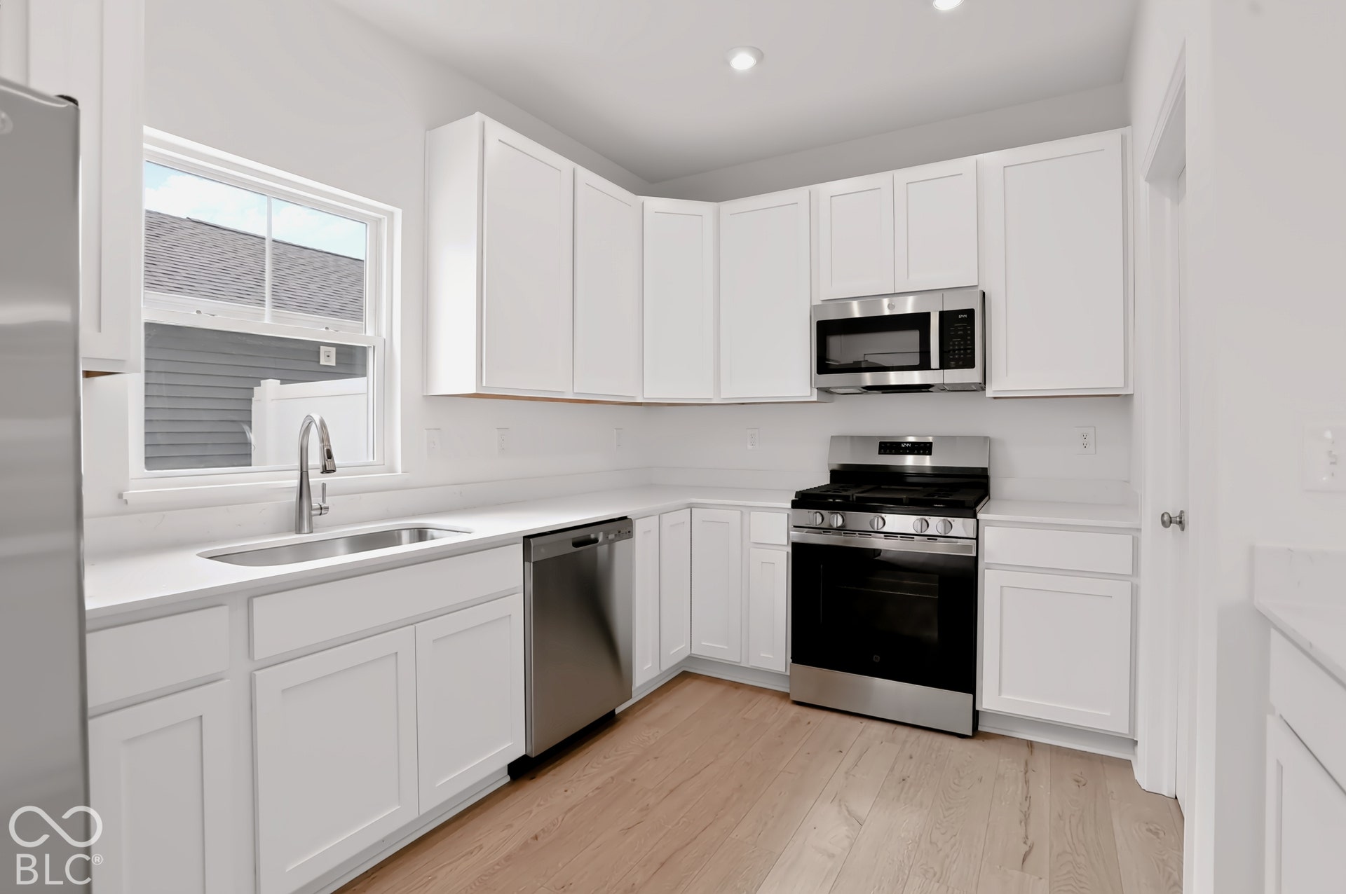 White shaker cabinetry, stainless steel appliances, wood-finish flooring, undermount sink, and recessed lighting