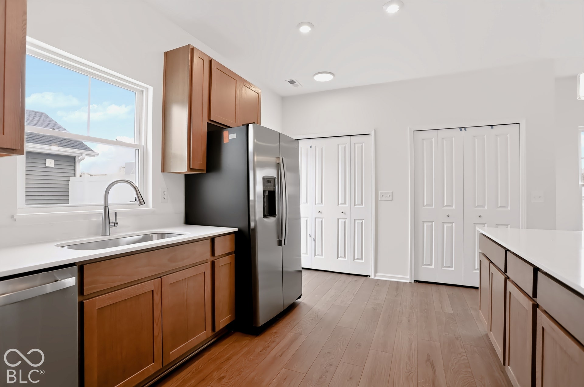 Kitchen featuring wood-finish flooring, white countertops, wood cabinetry, a stainless steel refrigerator, and recessed lighting