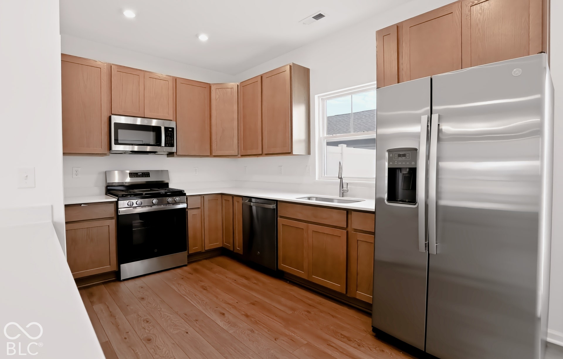 Kitchen featuring wood-finish cabinetry, stainless steel appliances, white countertops, a single basin sink, and wood-finish flooring