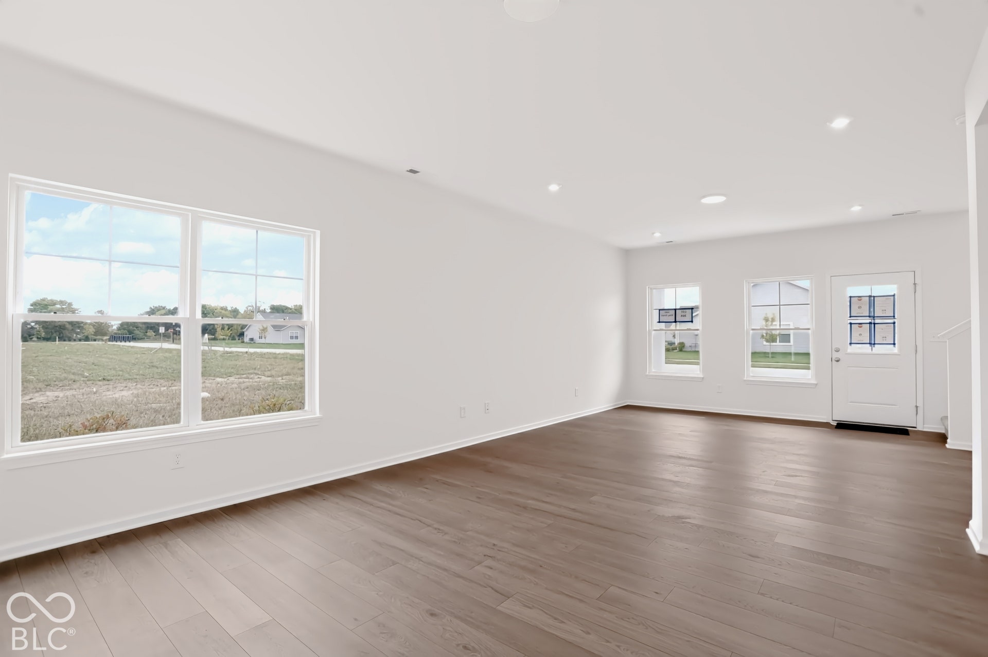 Spacious open-concept room featuring wood-finish flooring, recessed lighting, white walls, and multiple windows with white trim