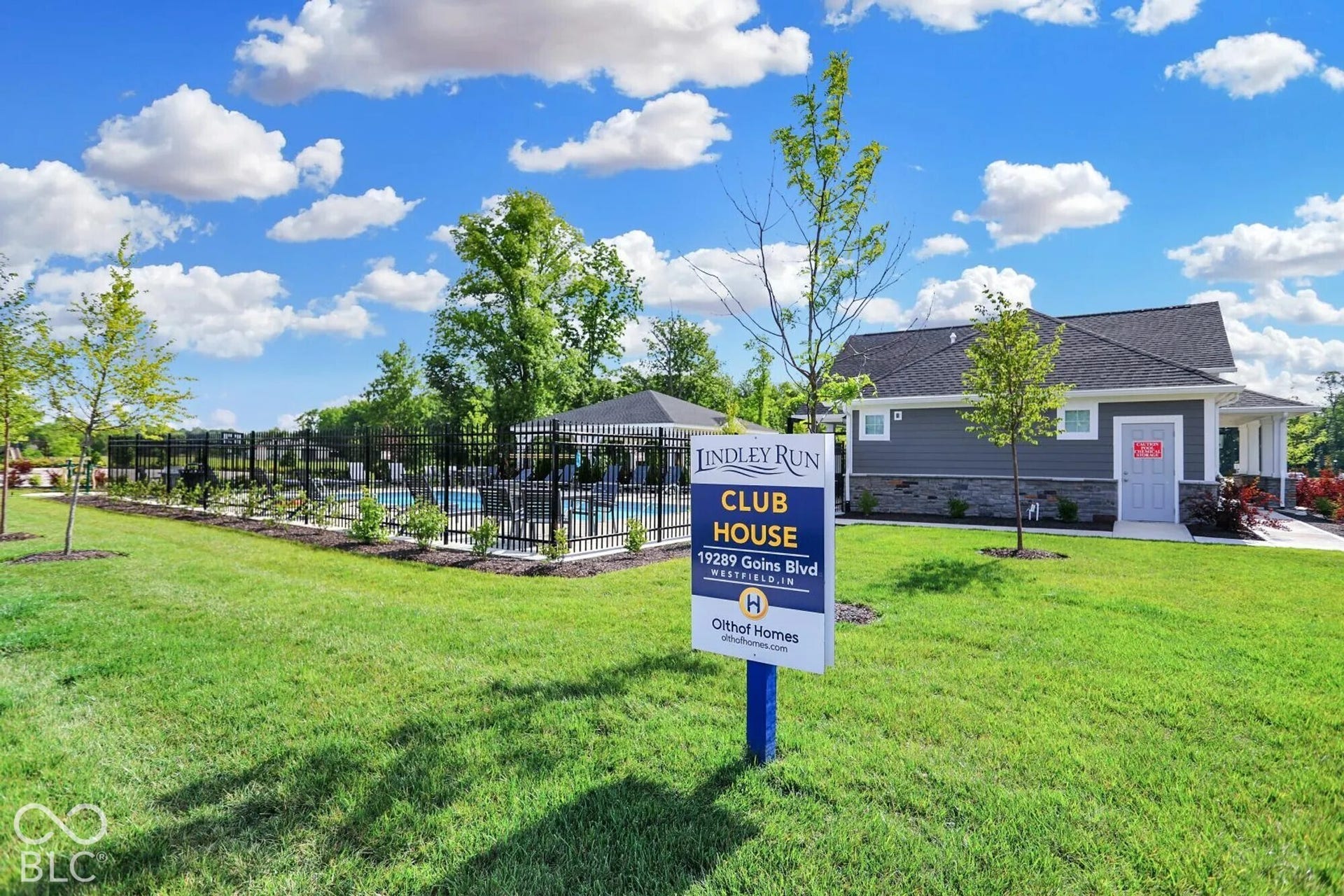 Community clubhouse with an outdoor swimming pool, black metal fencing, and landscaped grounds