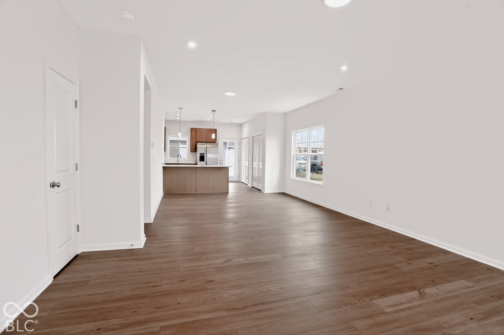 Open-concept living area with wood-finish flooring, recessed lighting, and a white interior color palette