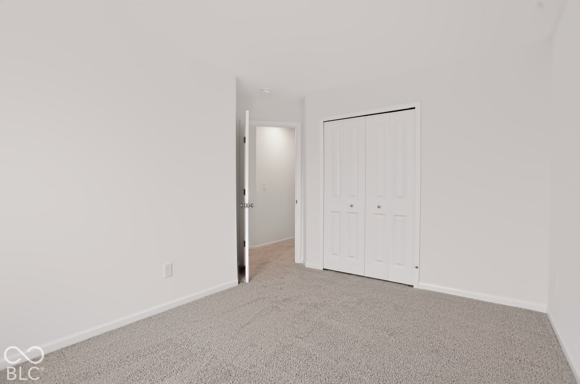 Plush gray carpeting, white walls, white bi-fold closet doors, and a white interior door