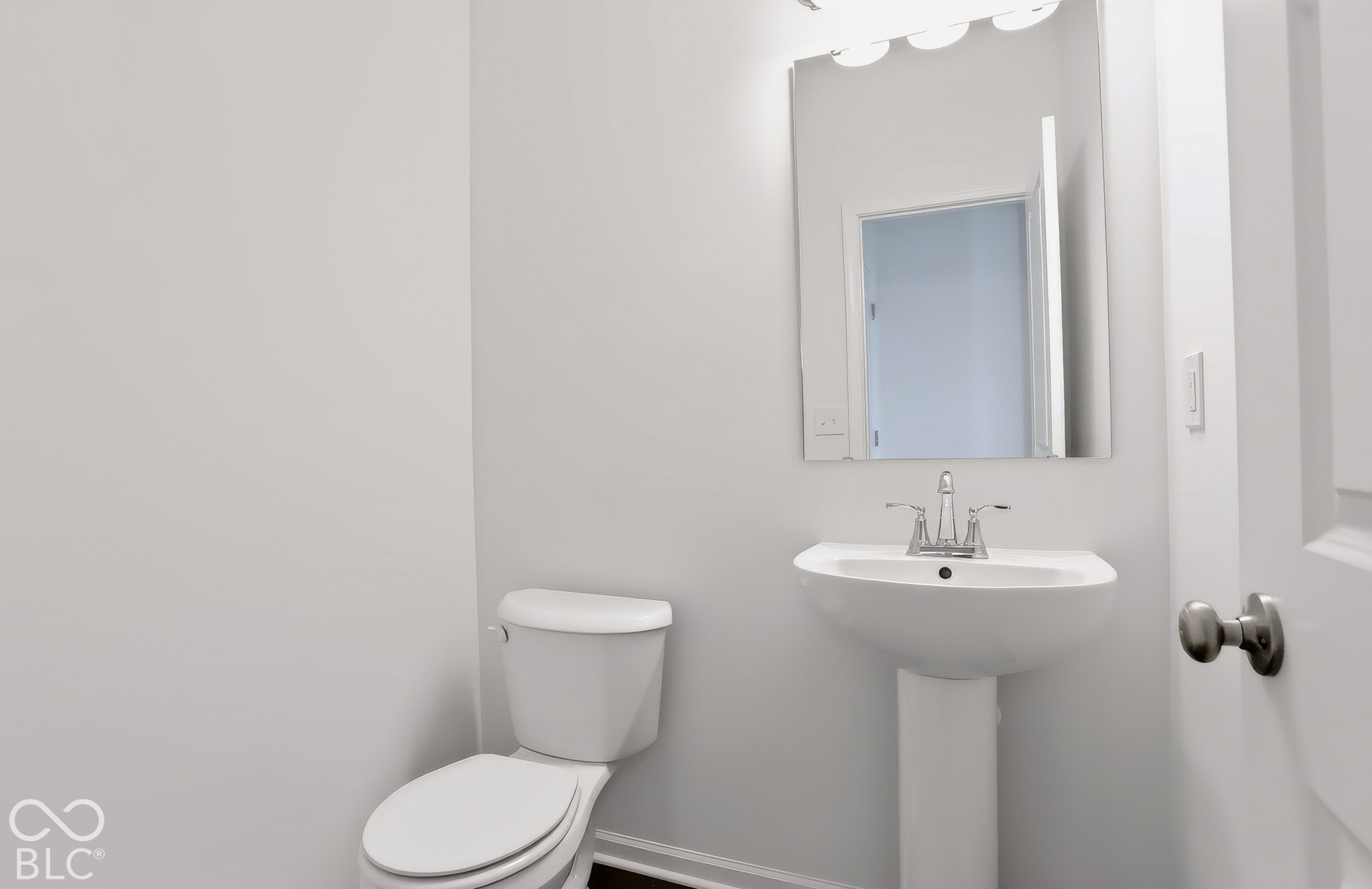 Ist floor half bath. Pedestal sink with chrome faucet, wall-mounted mirror, and overhead vanity lighting