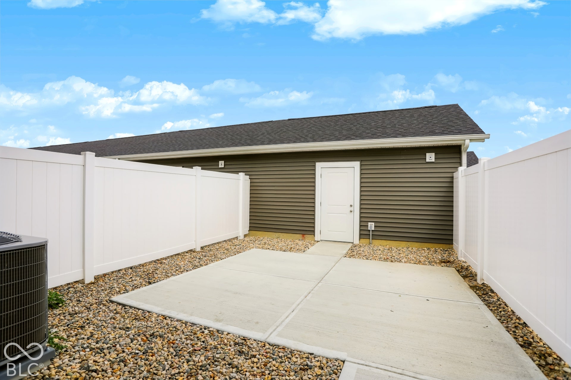 Concrete patio with gravel landscaping, white privacy fencing, and dark gray siding