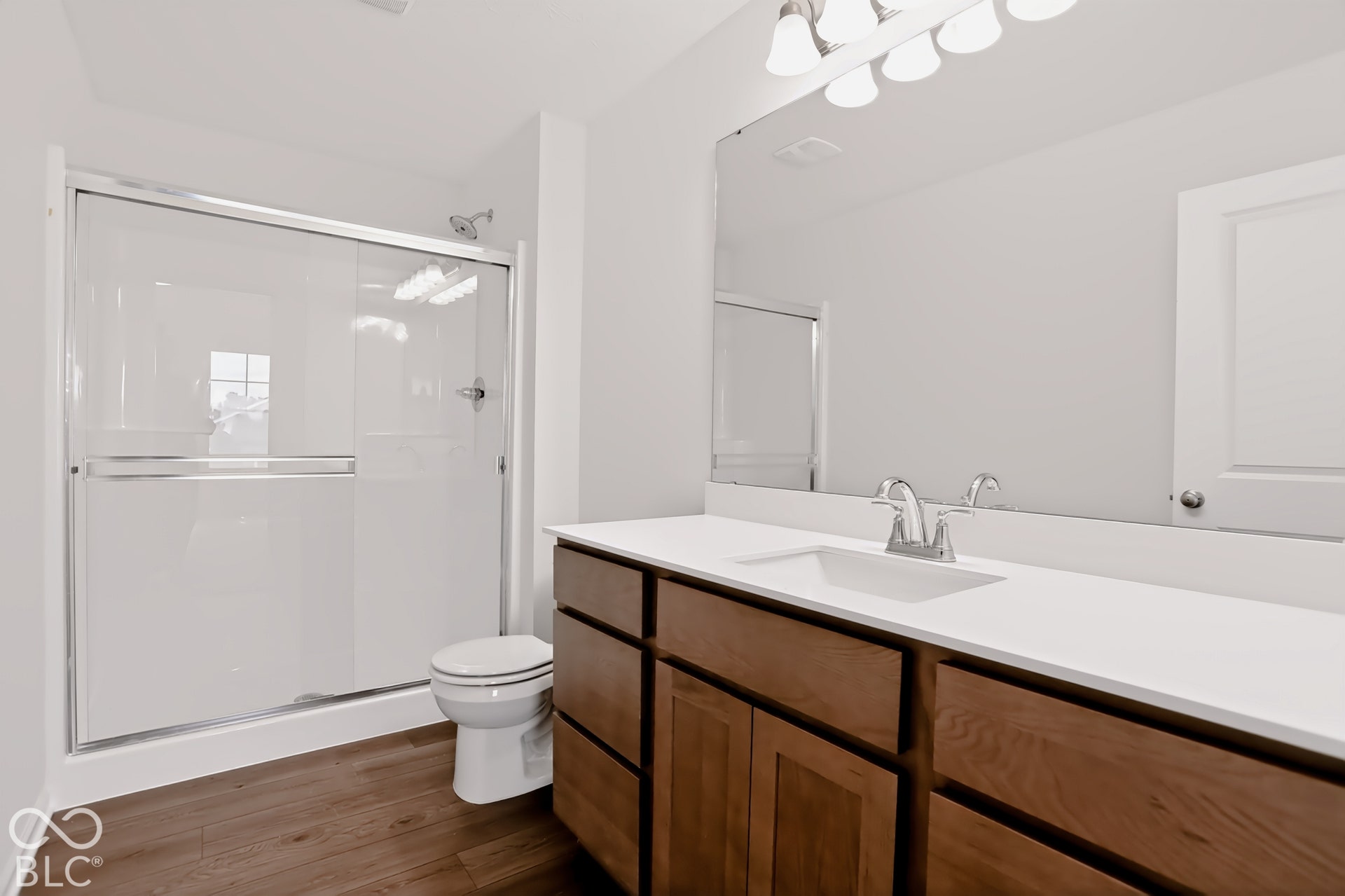 Primary Bath. Walk-in shower with sliding glass doors, single vanity with white countertop, integrated sink, chrome faucet, and wood-finish cabinetry