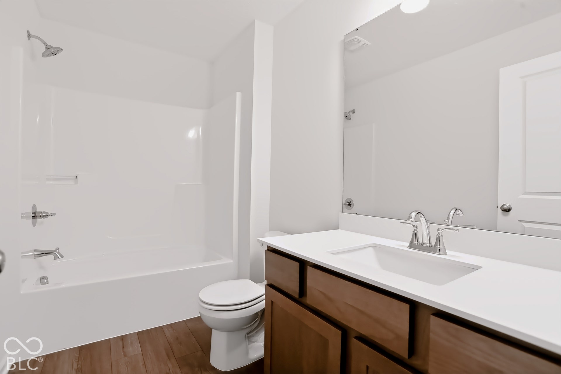 Wood-finish flooring, white vanity with an integrated sink, polished chrome faucet, and a wall-mounted mirror