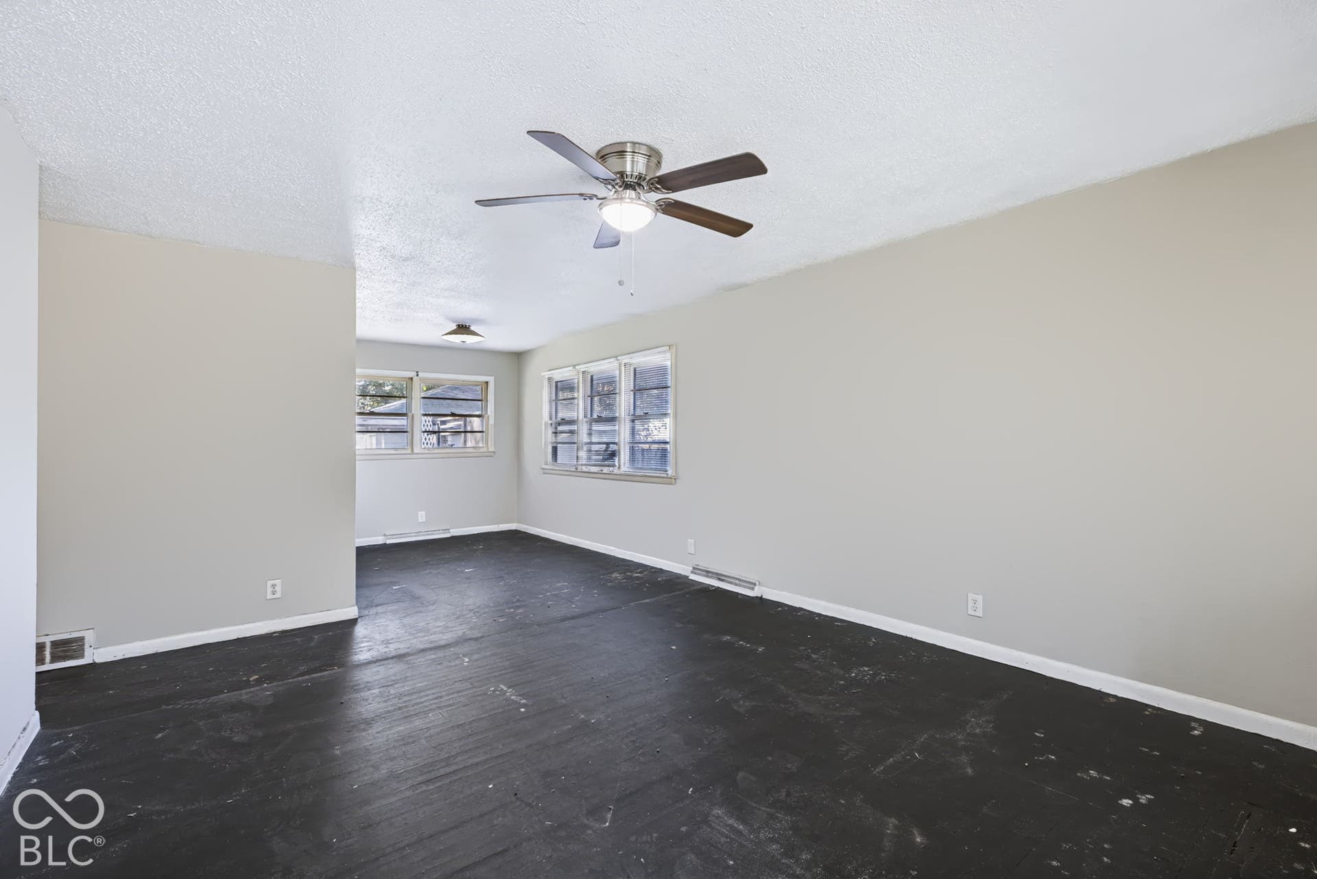 Spacious room with light neutral wall paint, overhead ceiling fan with light fixture, multiple windows, and dark wood-finish flooring
