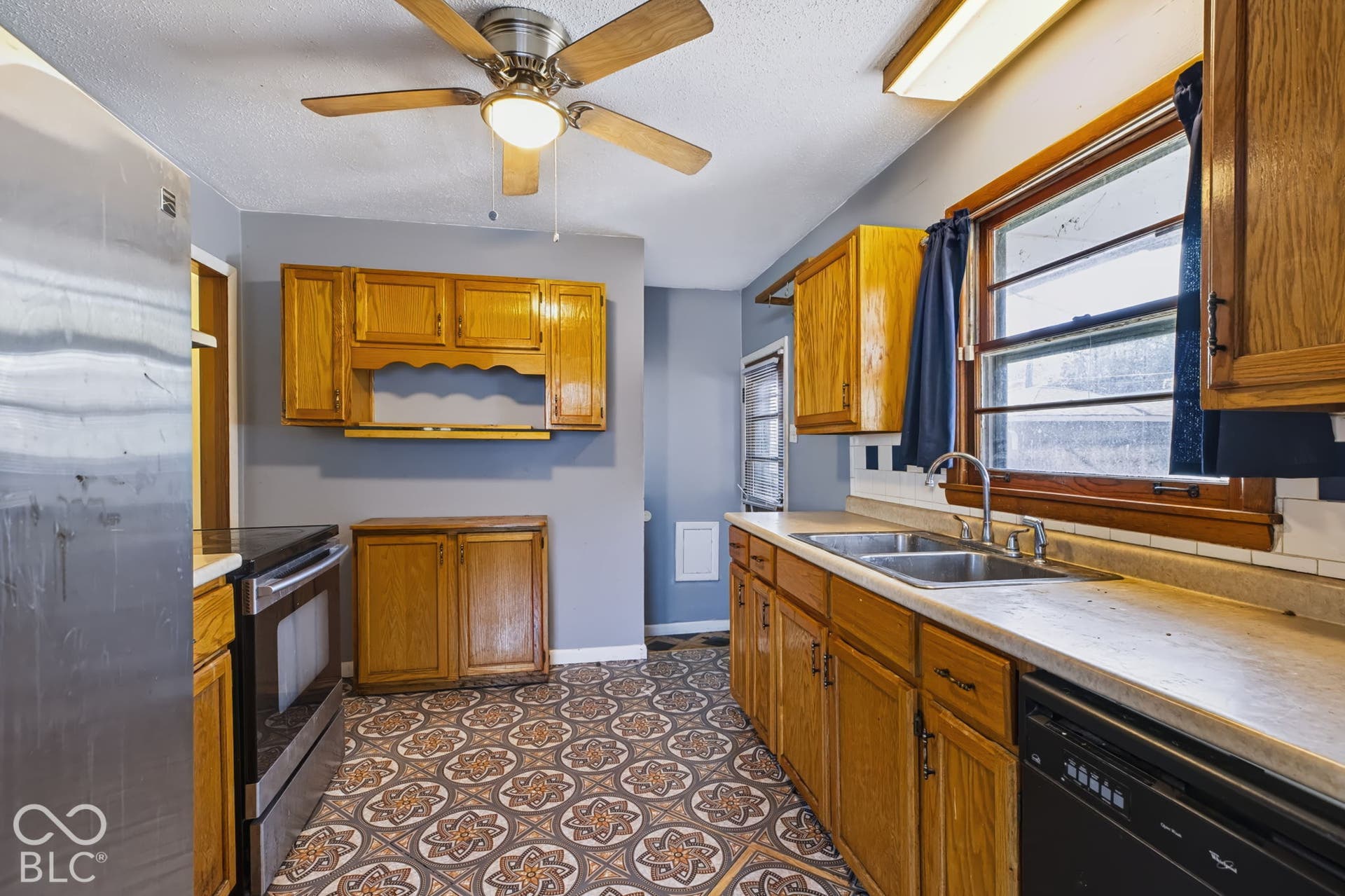Kitchen featuring wood cabinetry, patterned floor tiling, stainless steel appliances, and a ceiling fan with integrated lighting