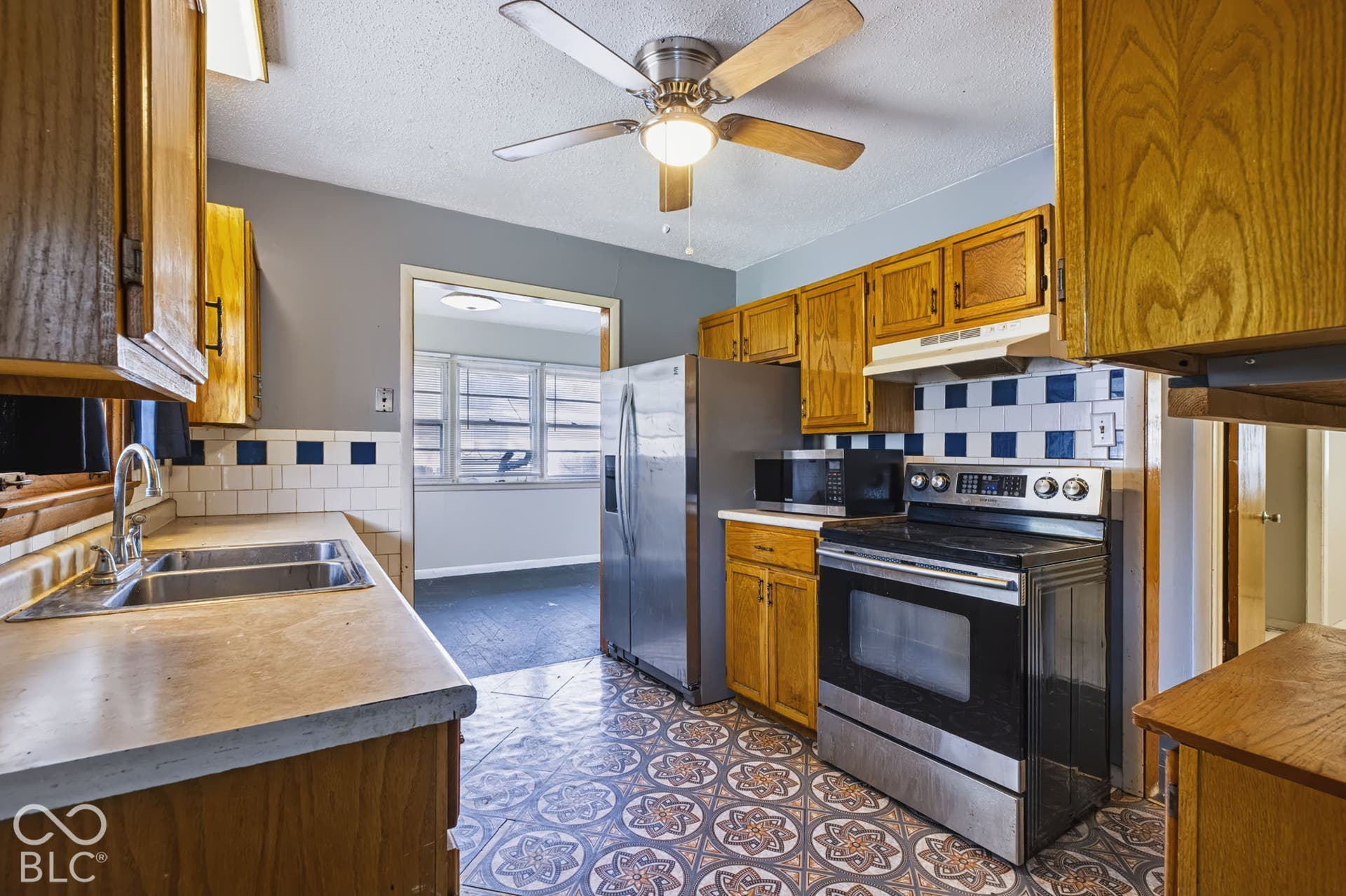 Kitchen featuring wood cabinetry, patterned floor tiles, a stainless steel electric range, and a dual-basin sink