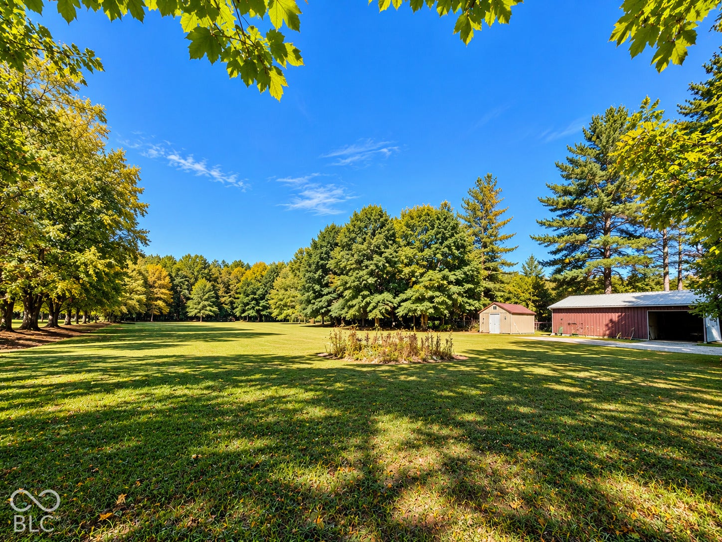 3680 S State Road 75, Coatesville, IN 46121 Expansive green lawn surrounded by mature trees, featuring a red barn-style outbuilding and an additional utility shed