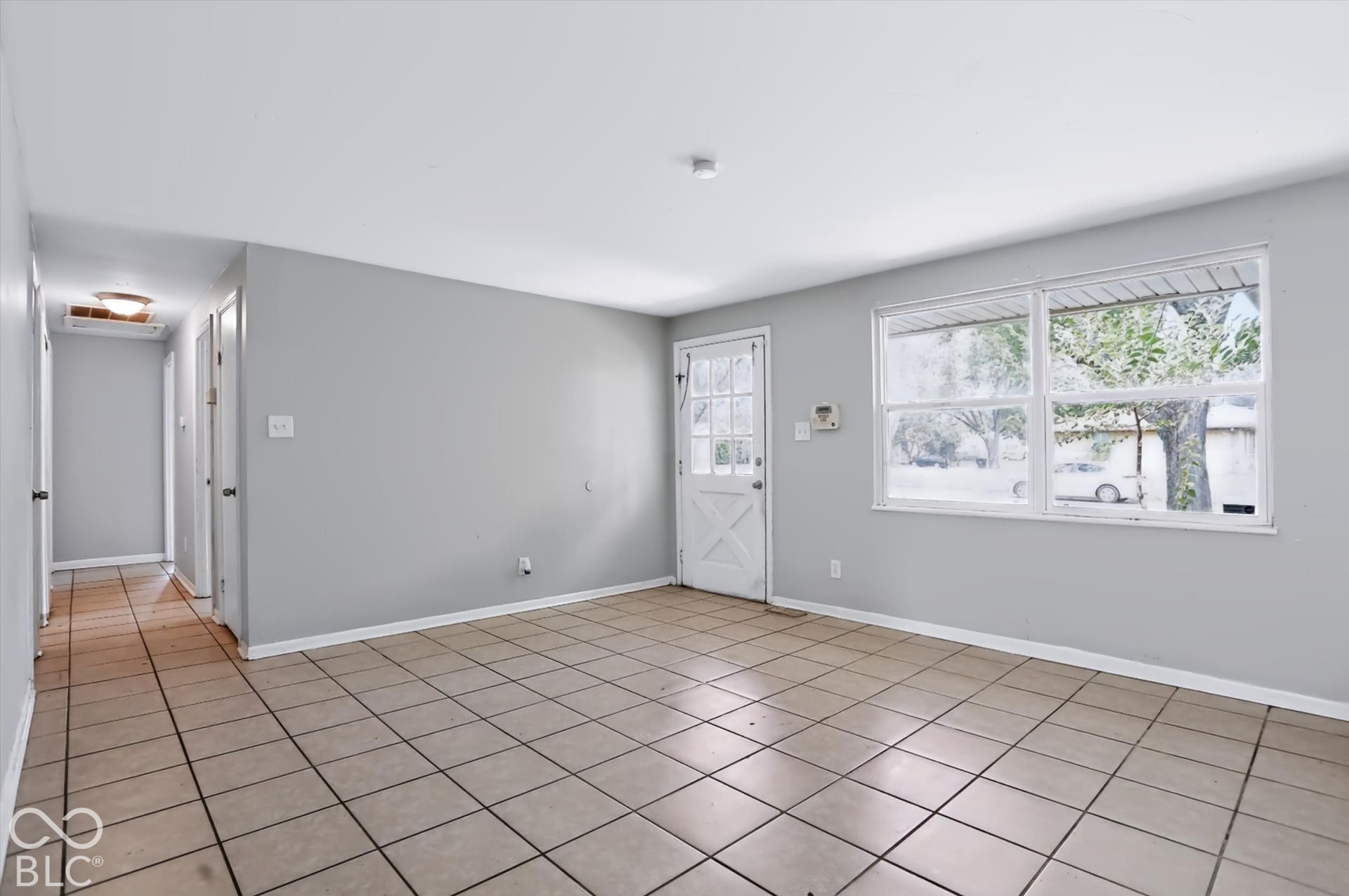 Spacious interior with tile flooring, a white paneled door with windowpanes, and large windows