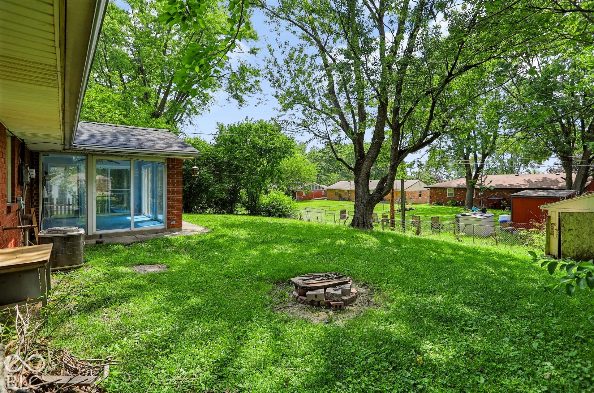 Backyard featuring a sunroom, brick exterior, mature trees, and a grassy lawn