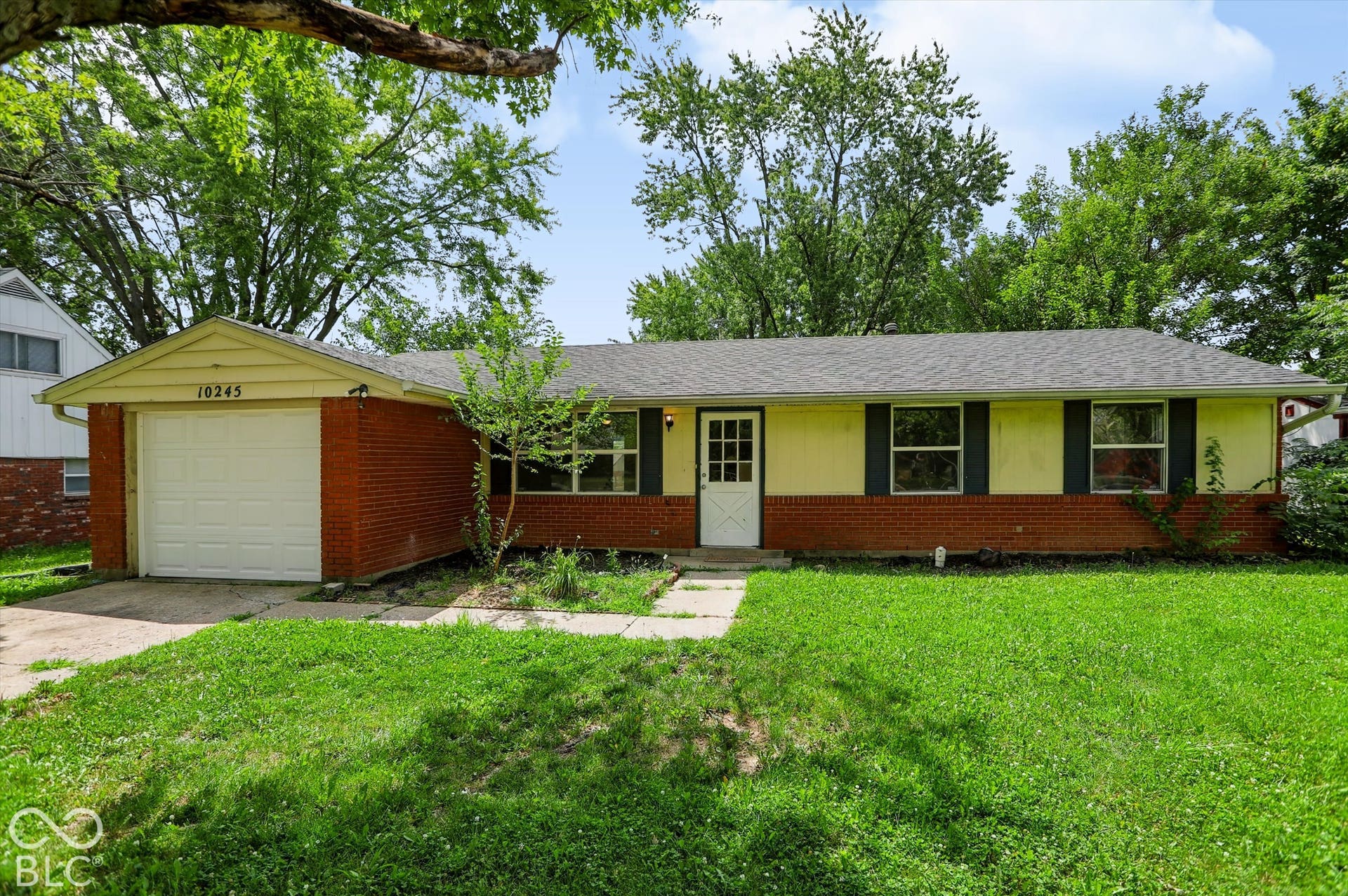 Brick and siding exterior with dark shutters, an attached garage, a front entry door with glass panels, and a concrete pathway