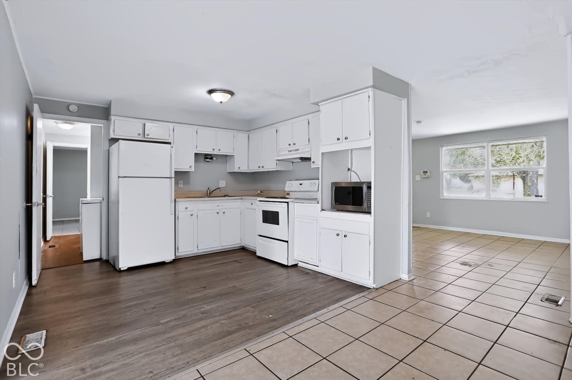 Kitchen featuring white cabinetry, white appliances, wood-finish flooring, and tile flooring