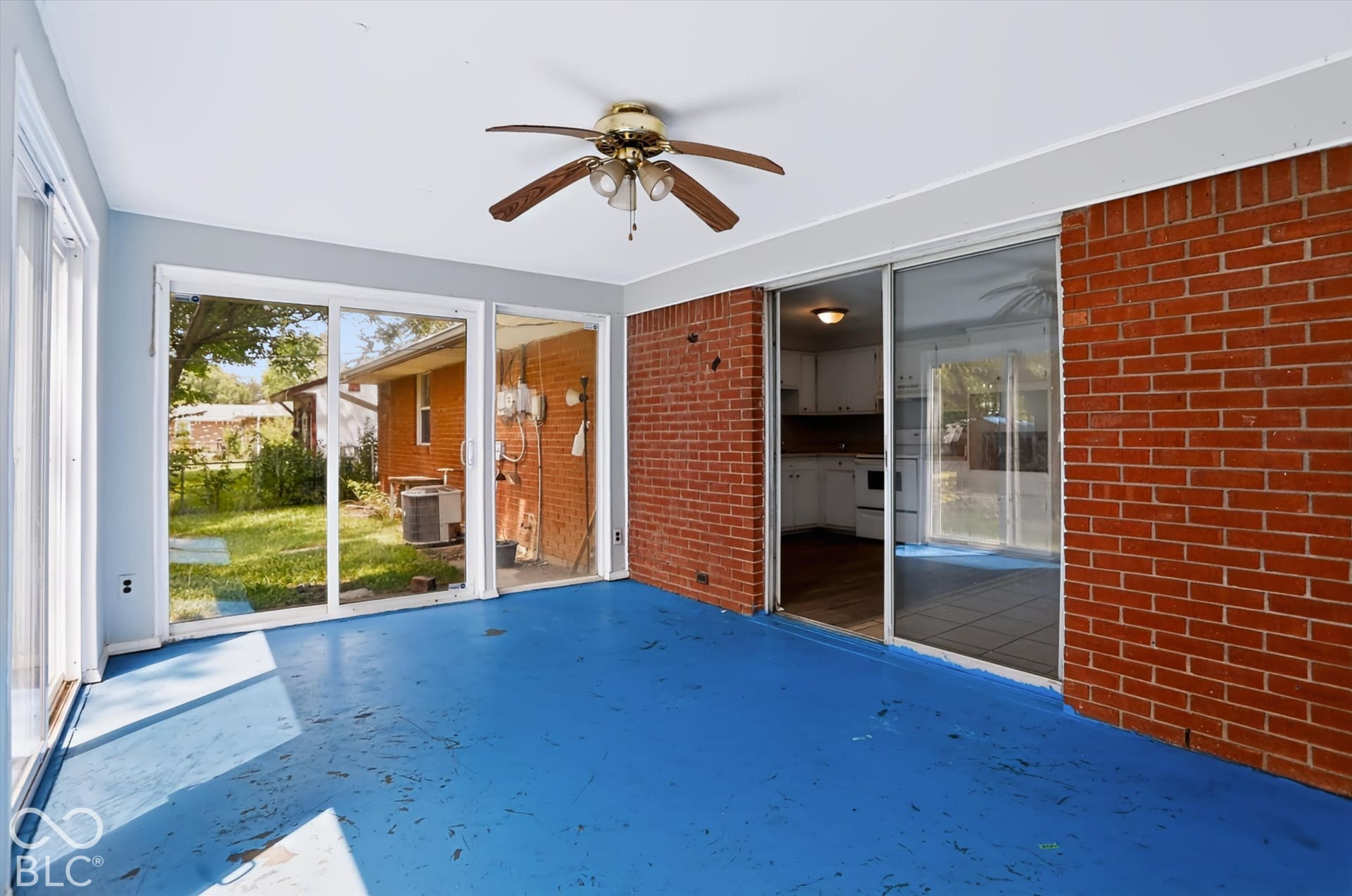 Enclosed space with a ceiling fan, brick accent wall, and multiple sliding glass doors